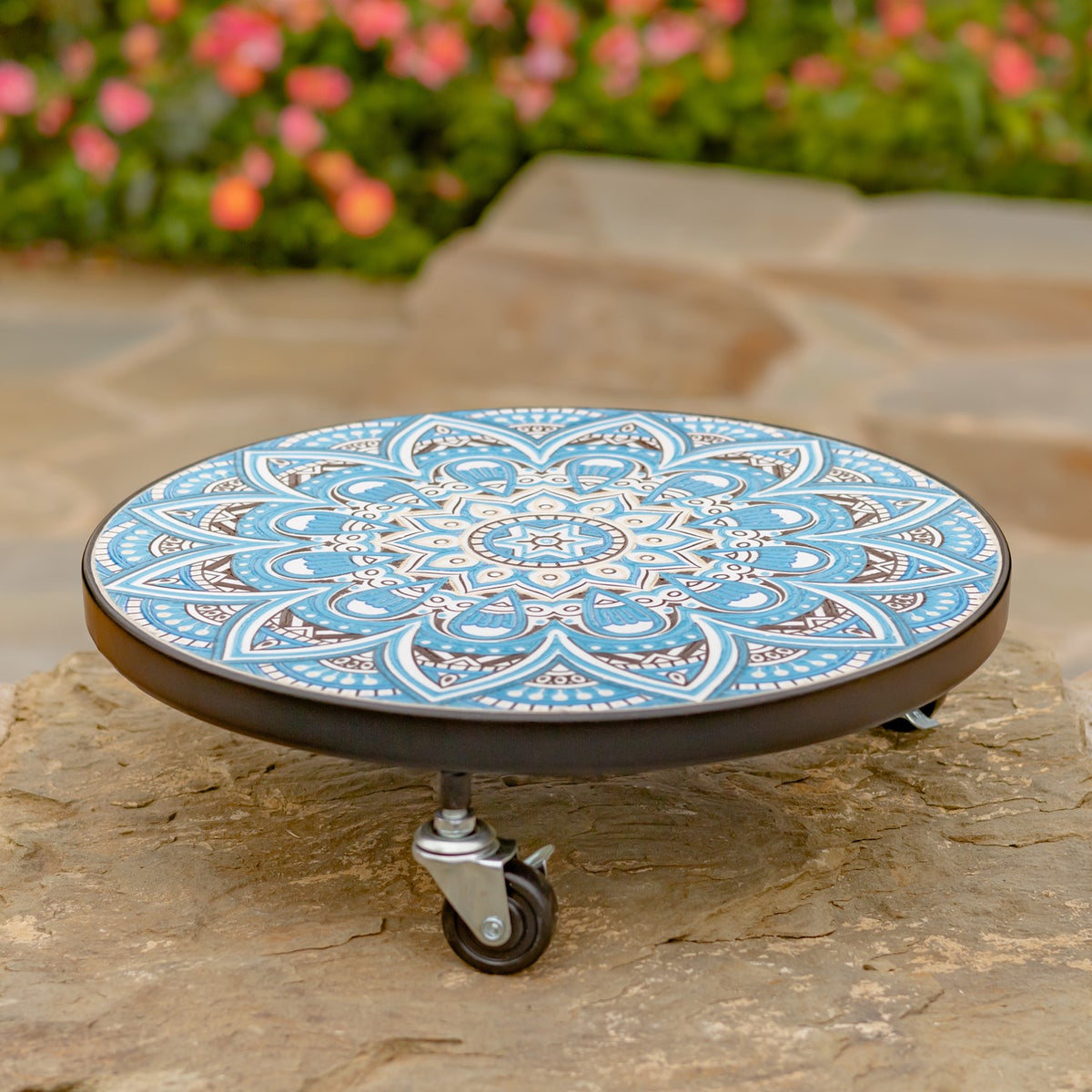 Round plant trolley with a blue-and-white patterned top and dark rim on caster wheels outdoors.