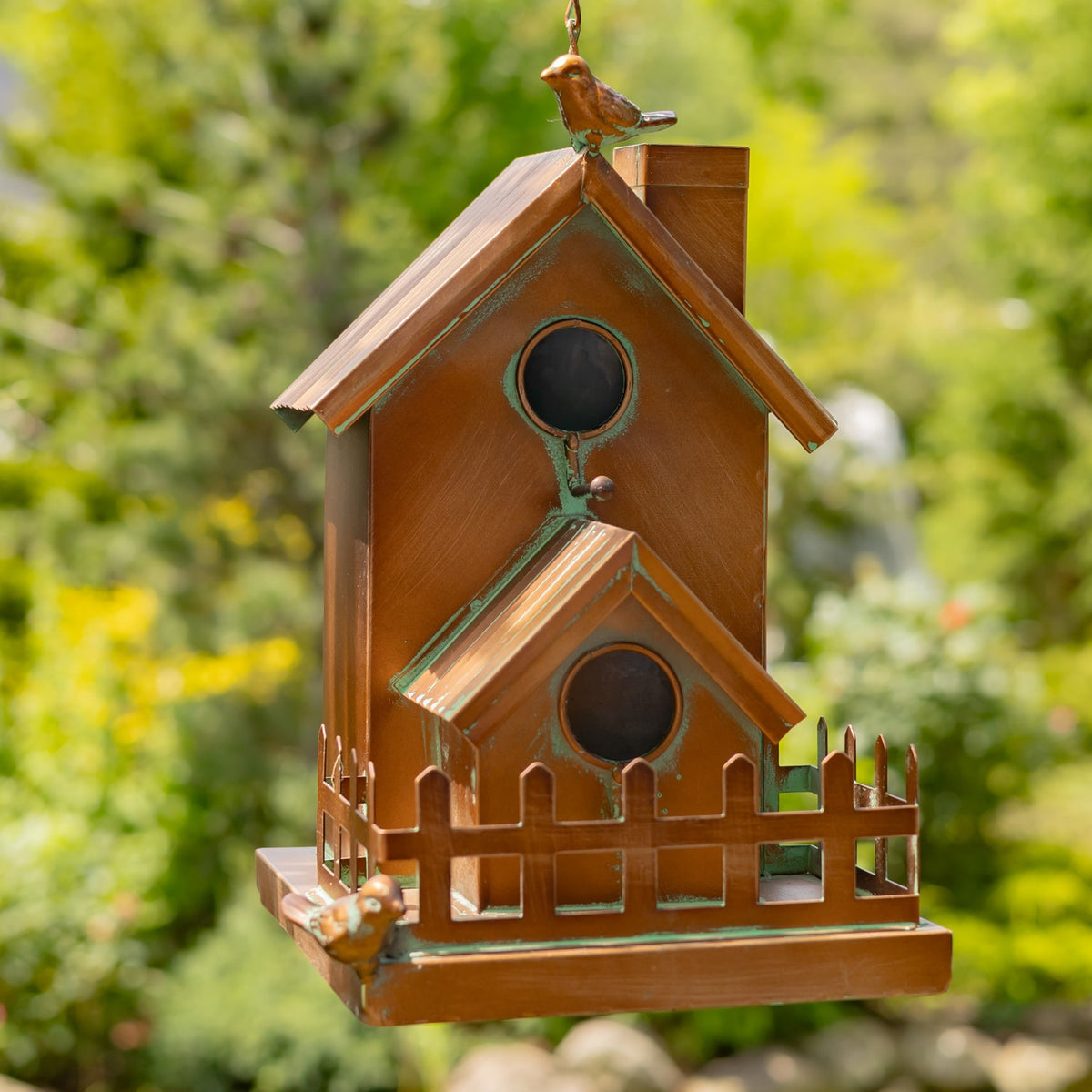 Copper-toned hanging birdhouse with two round openings, a small fence, and decorative metal birds.