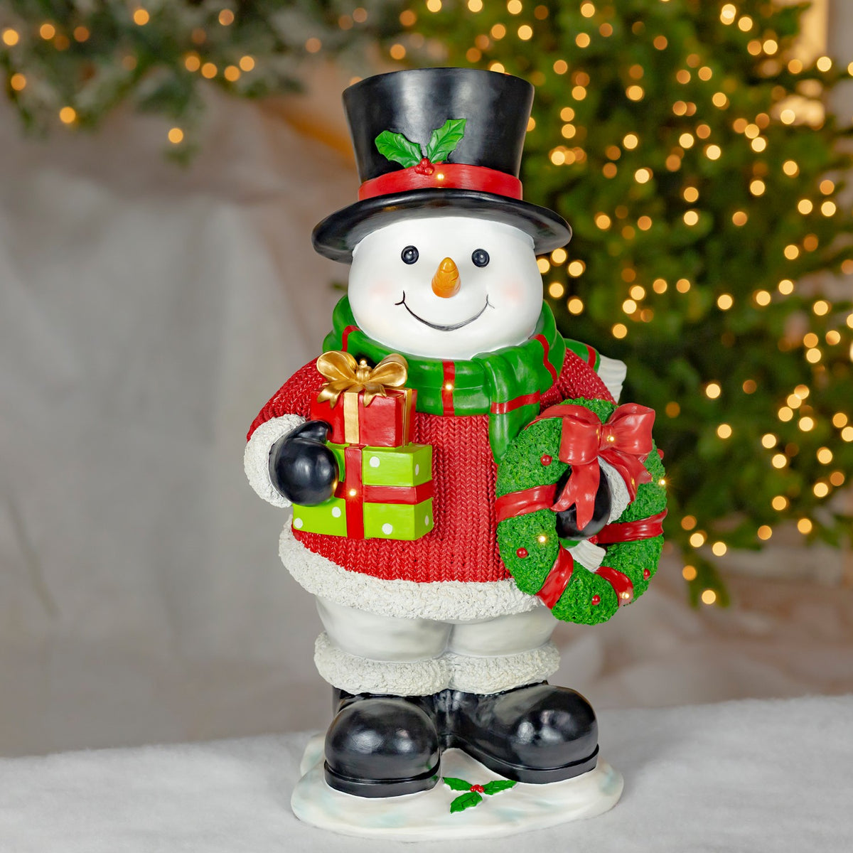 Full snowman decoration in a top hat, red sweater and green scarf, holding gifts and a wreath.