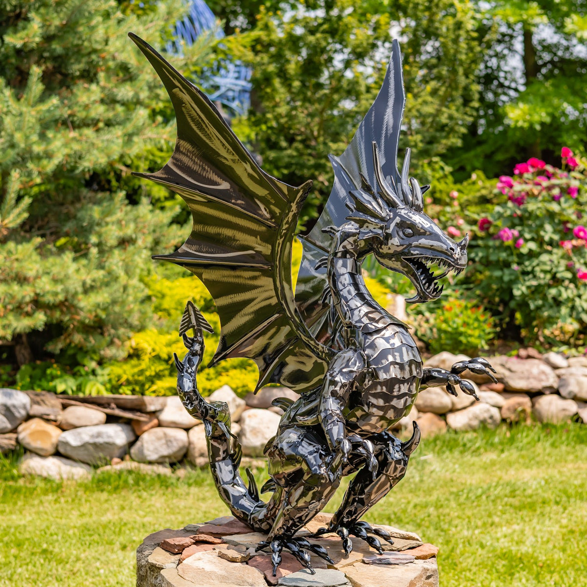 Upright metal dragon statue with spread wings on a stone pedestal in a garden