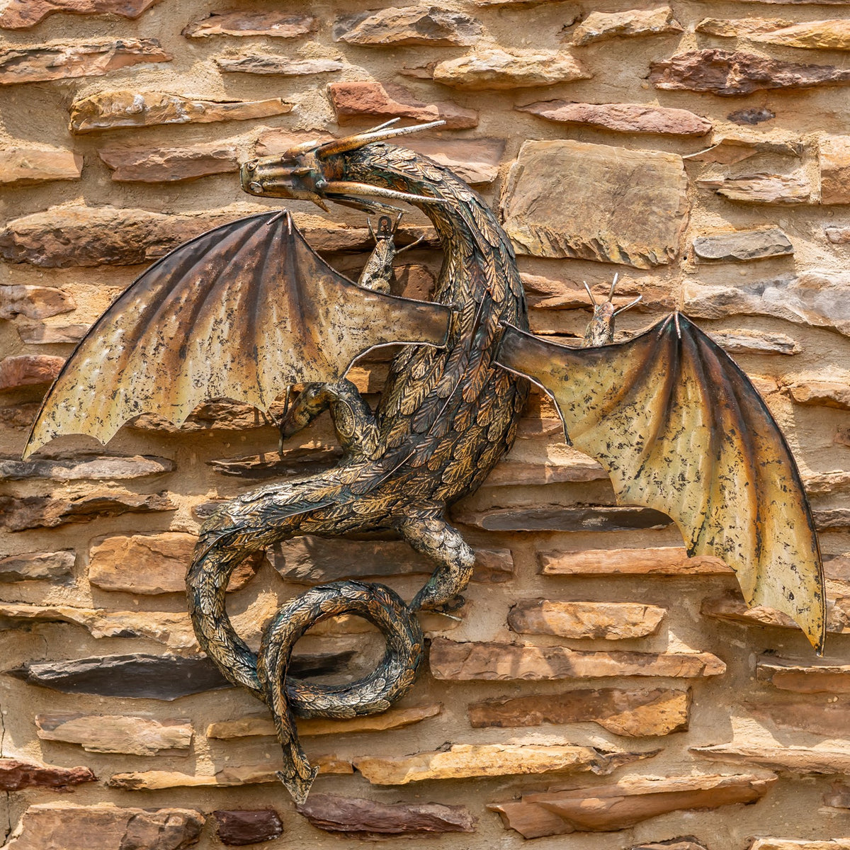 Metal dragon wall decoration with outstretched wings and a coiled tail against a stone wall.