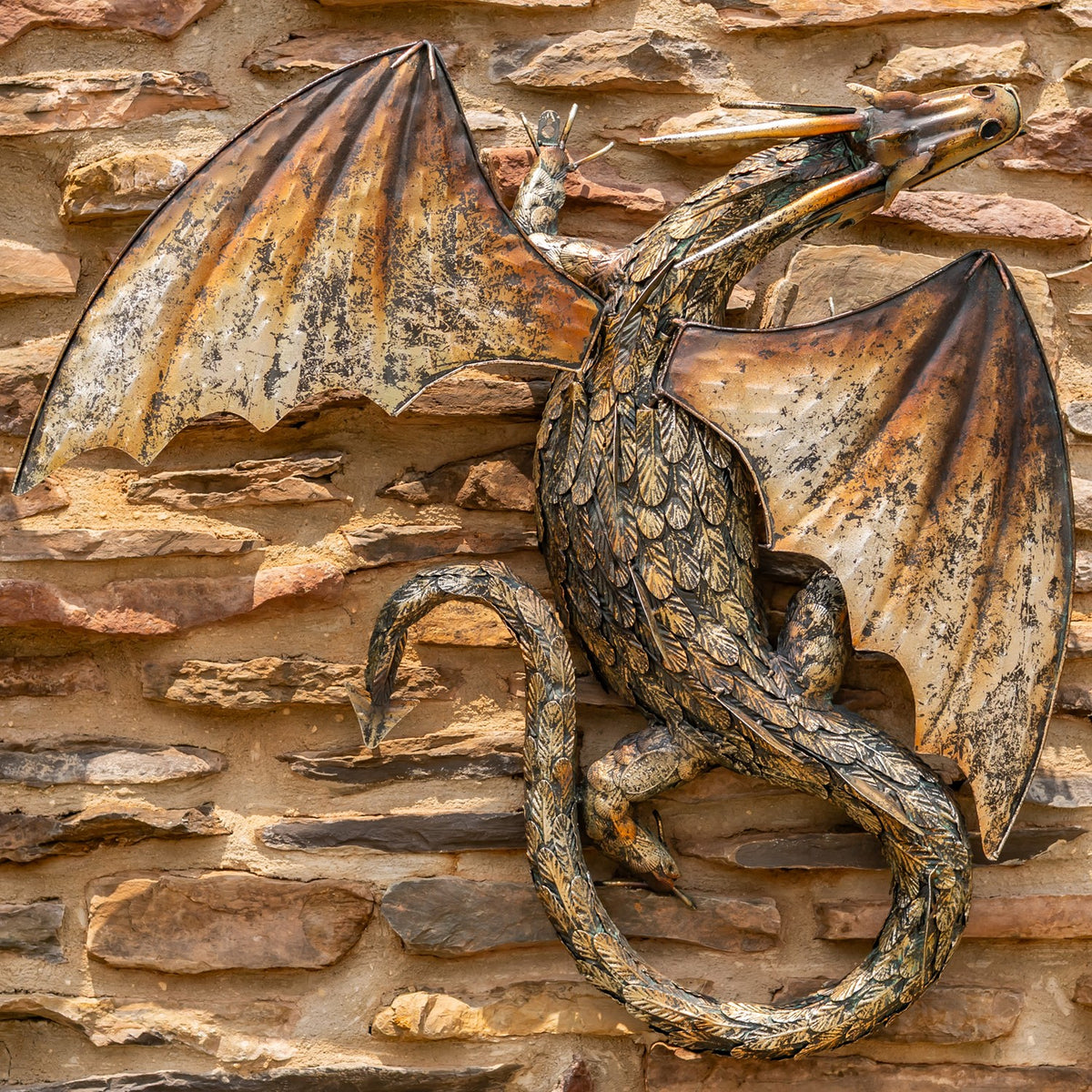 Metal dragon wall sculpture with spread wings and curled tail against a layered stone wall.