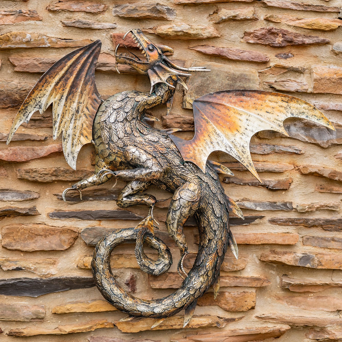 Bronze-toned metal dragon with spread wings and curled tail mounted on a stone wall.