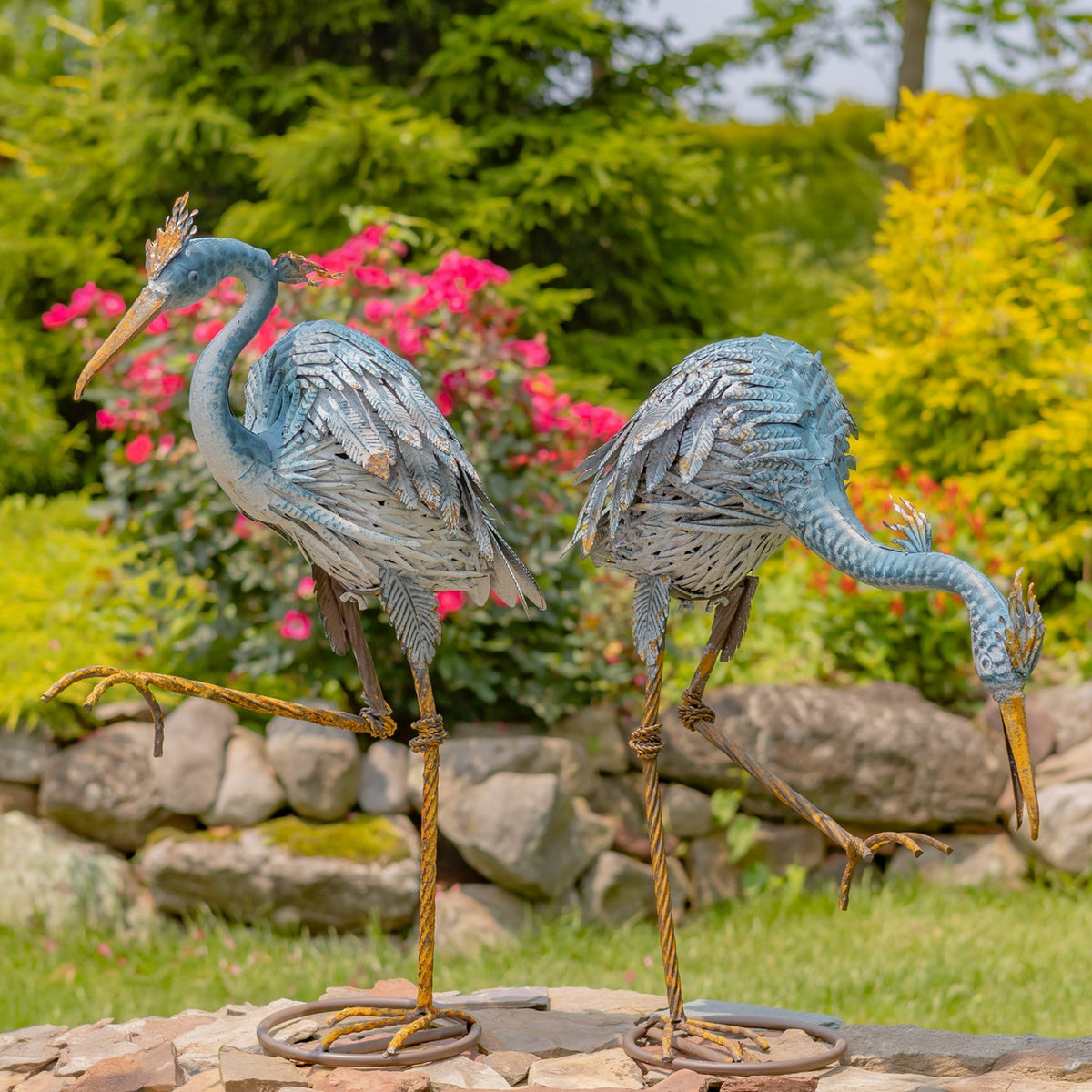 Pair of blue and grey heron figurines standing on circular bases in a garden