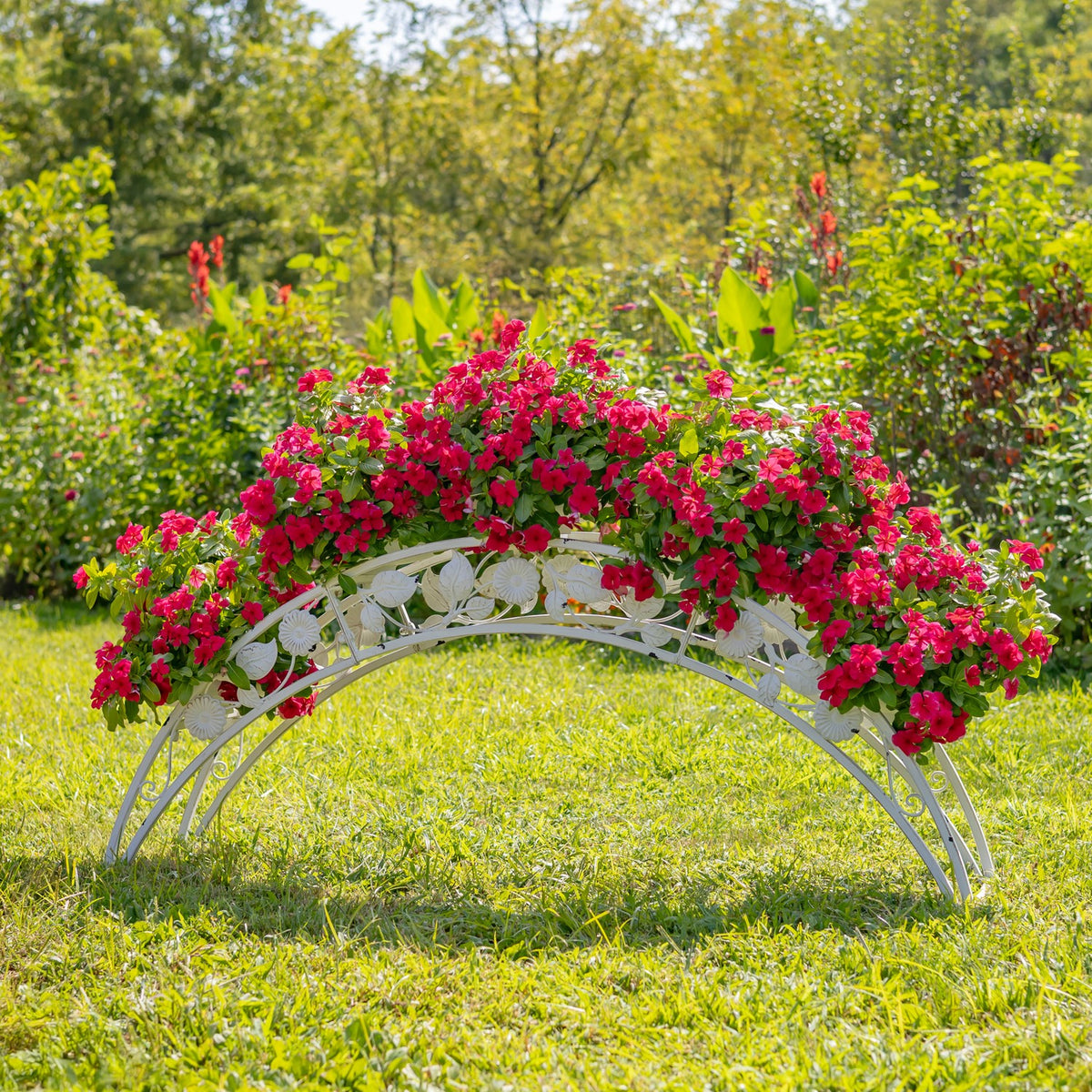 White arched metal plant stand filled with pink flowers on a lawn