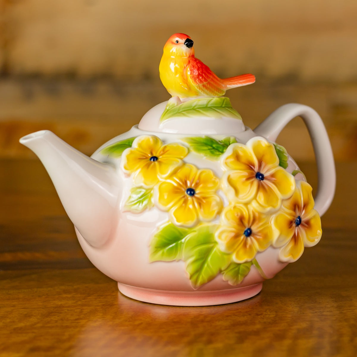 White teapot with raised yellow flowers and green leaves, topped with a colorful bird figurine.