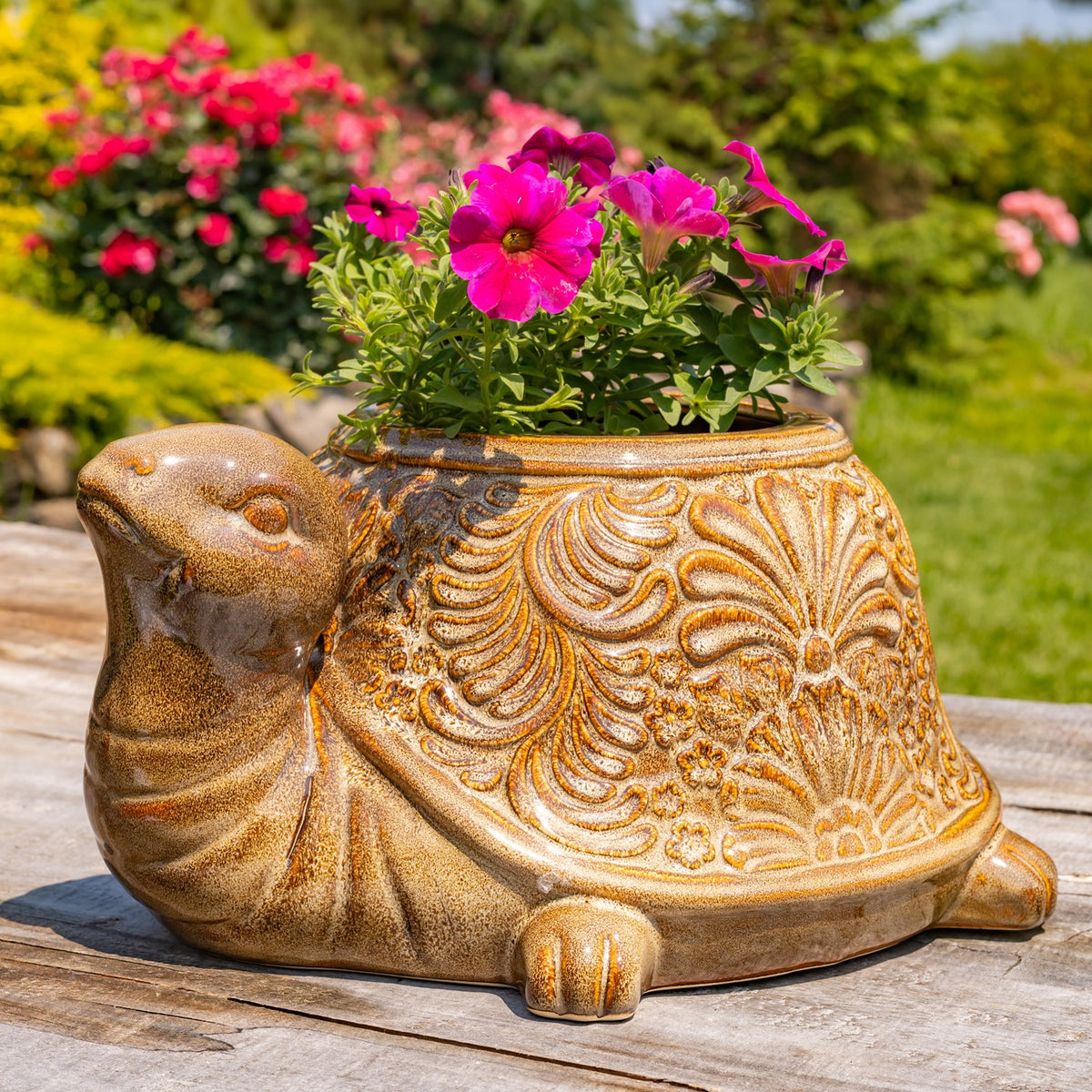 Flower-filled turtle planter with an ornate golden-brown shell on a sunny wooden deck.