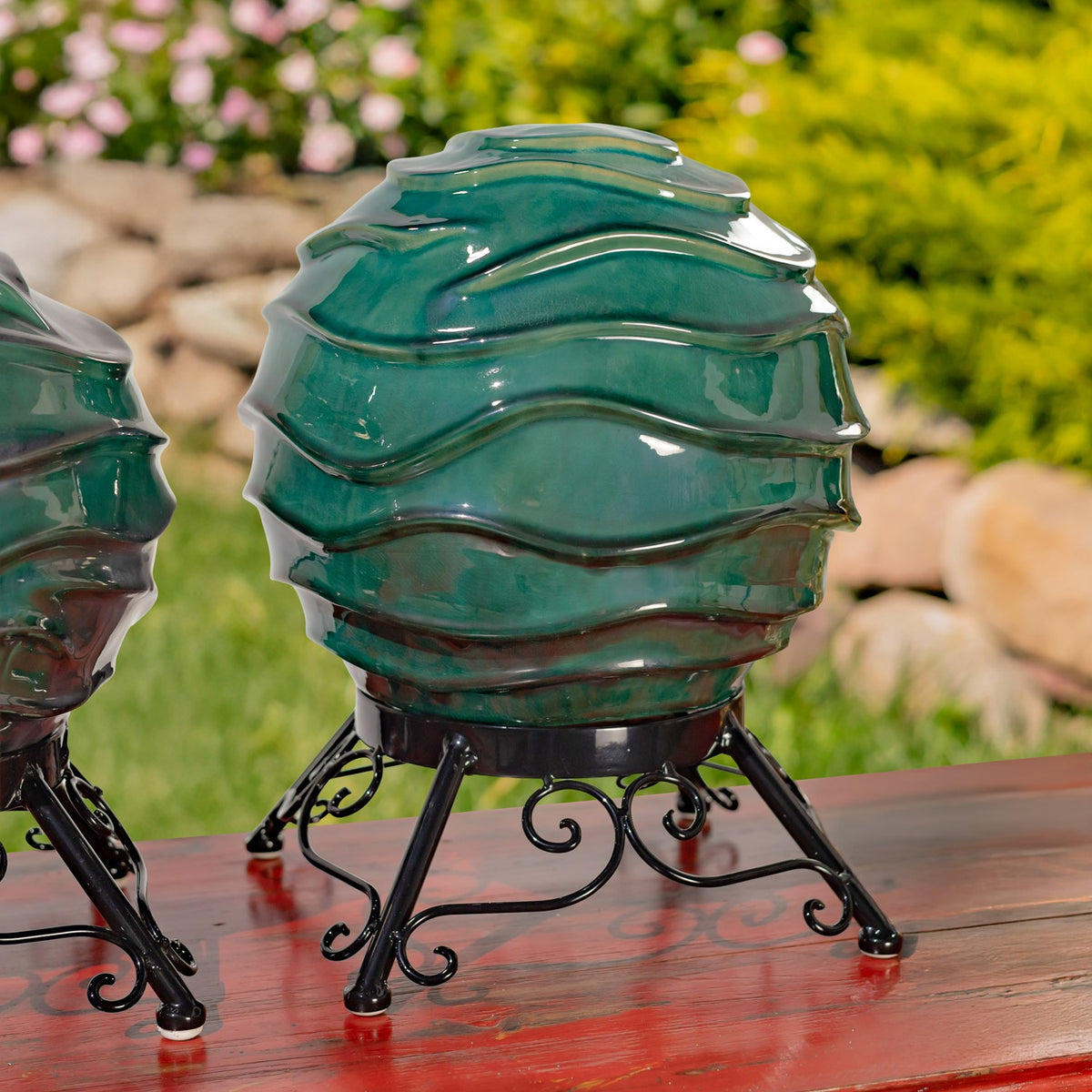 Large glossy teal globe with layered ridges on a black scrollwork stand, with part of another globe beside it.
