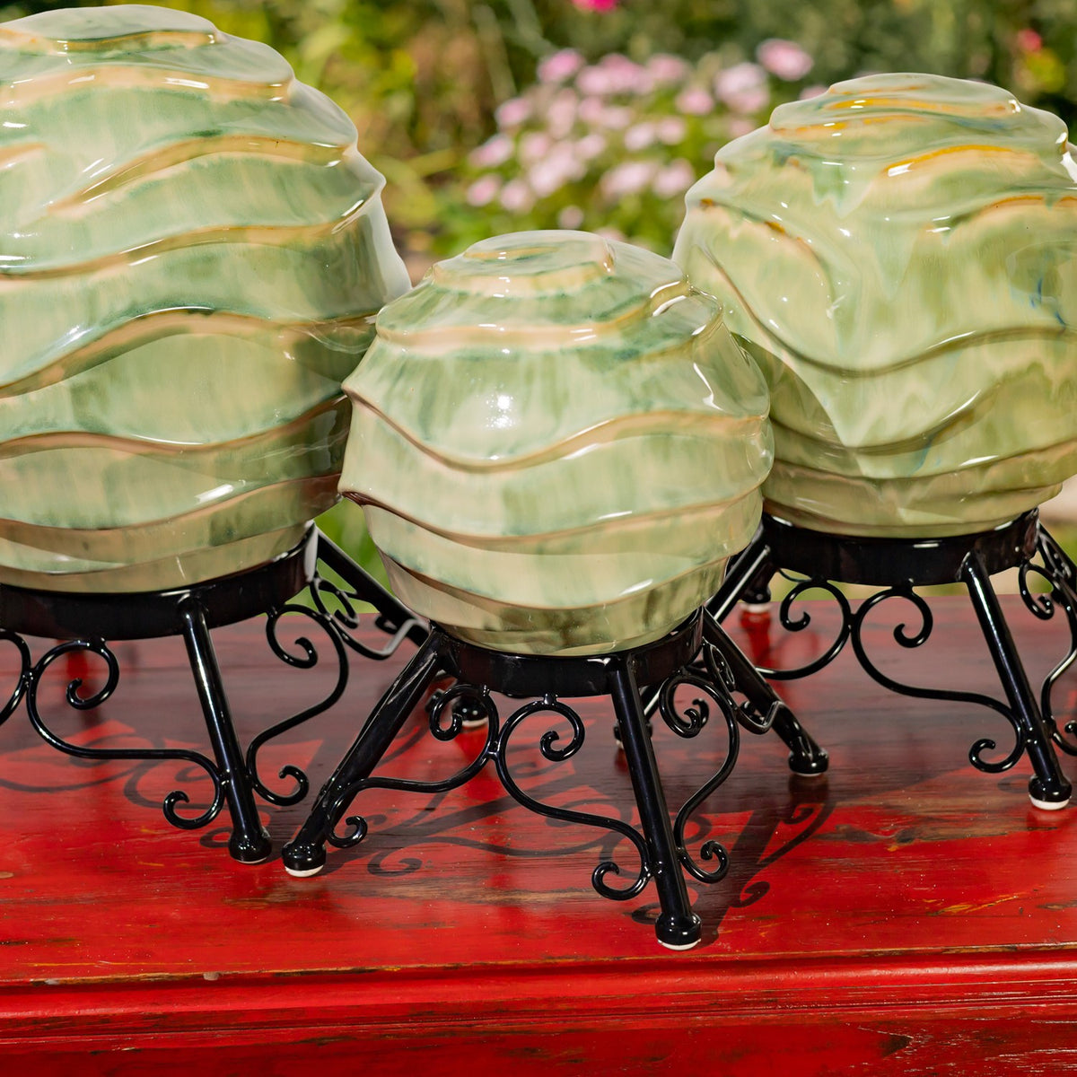 Three pale green glazed globes with raised wavy bands on black scrollwork stands, shown close up on a red table.