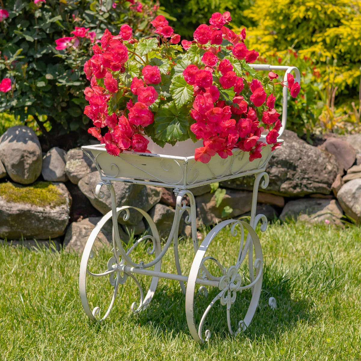 Antique-white metal flower cart filled with bright pink flowers on a garden lawn.