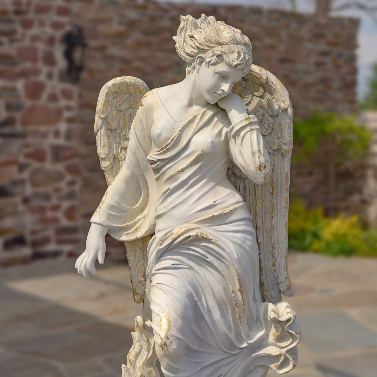 A seated angel statue with flowing robes and spread wings, shown against a brick wall.