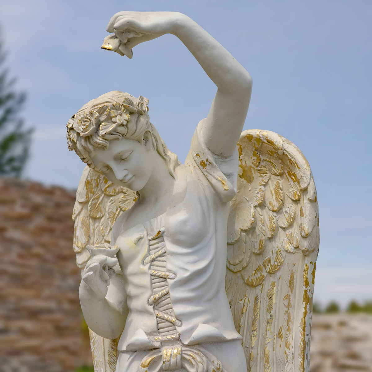 Close view of the angel statue’s bowed face, raised arm, and weathered wings with gold-toned accents.