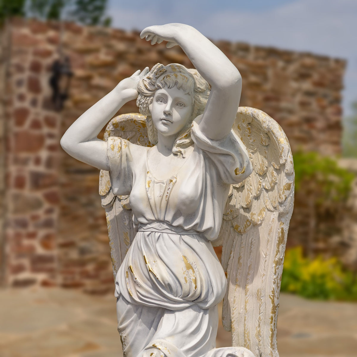 Close view of a pale angel statue with raised arms, carved wings, and gold-toned weathering.