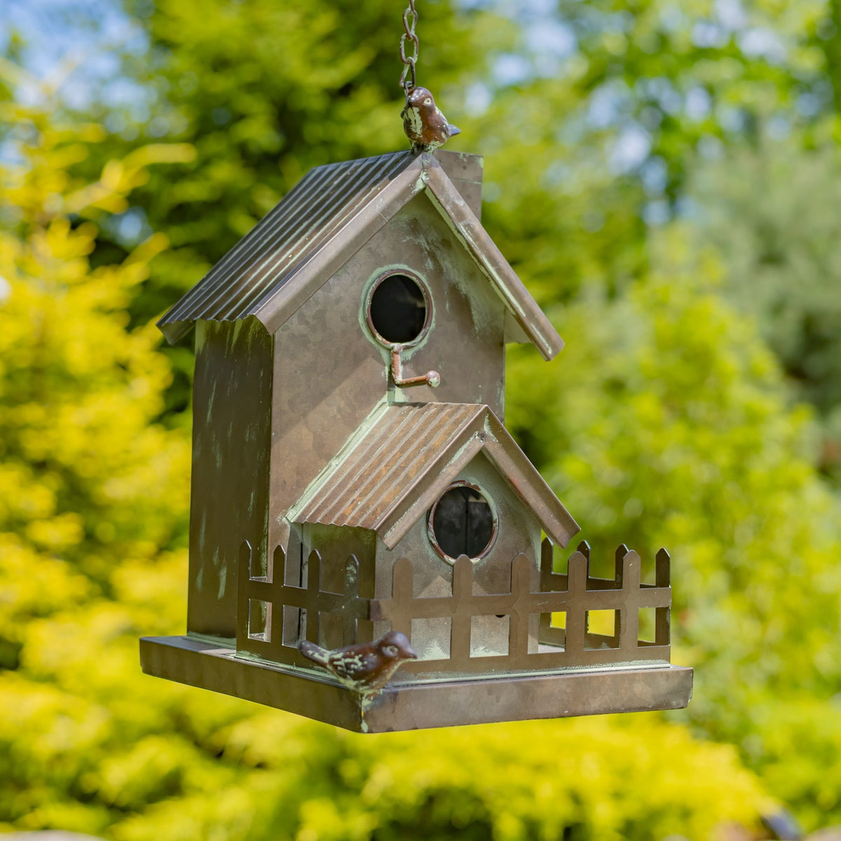 Hanging metal birdhouse with two gabled sections, round openings, a small fence, and decorative birds.