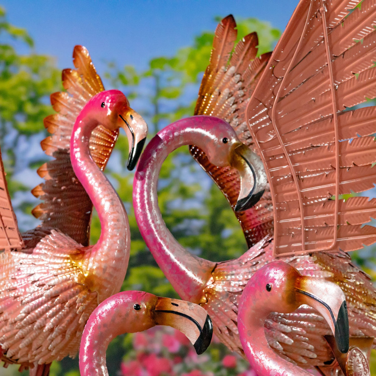 Close-up of several pink metal flamingos, showing textured wings and curved beaks.