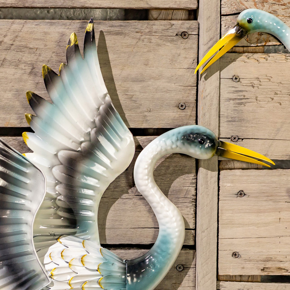 Close-up of a painted crane wall decoration, showing its curved neck, yellow beak, and layered wing feathers.