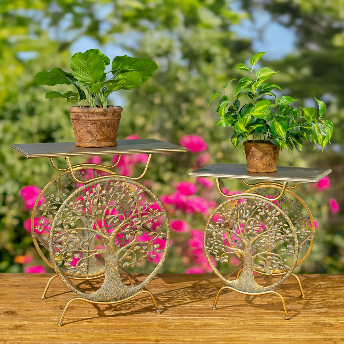 Two gold tree-of-life plant stands with potted plants on a wooden deck in a flower garden.