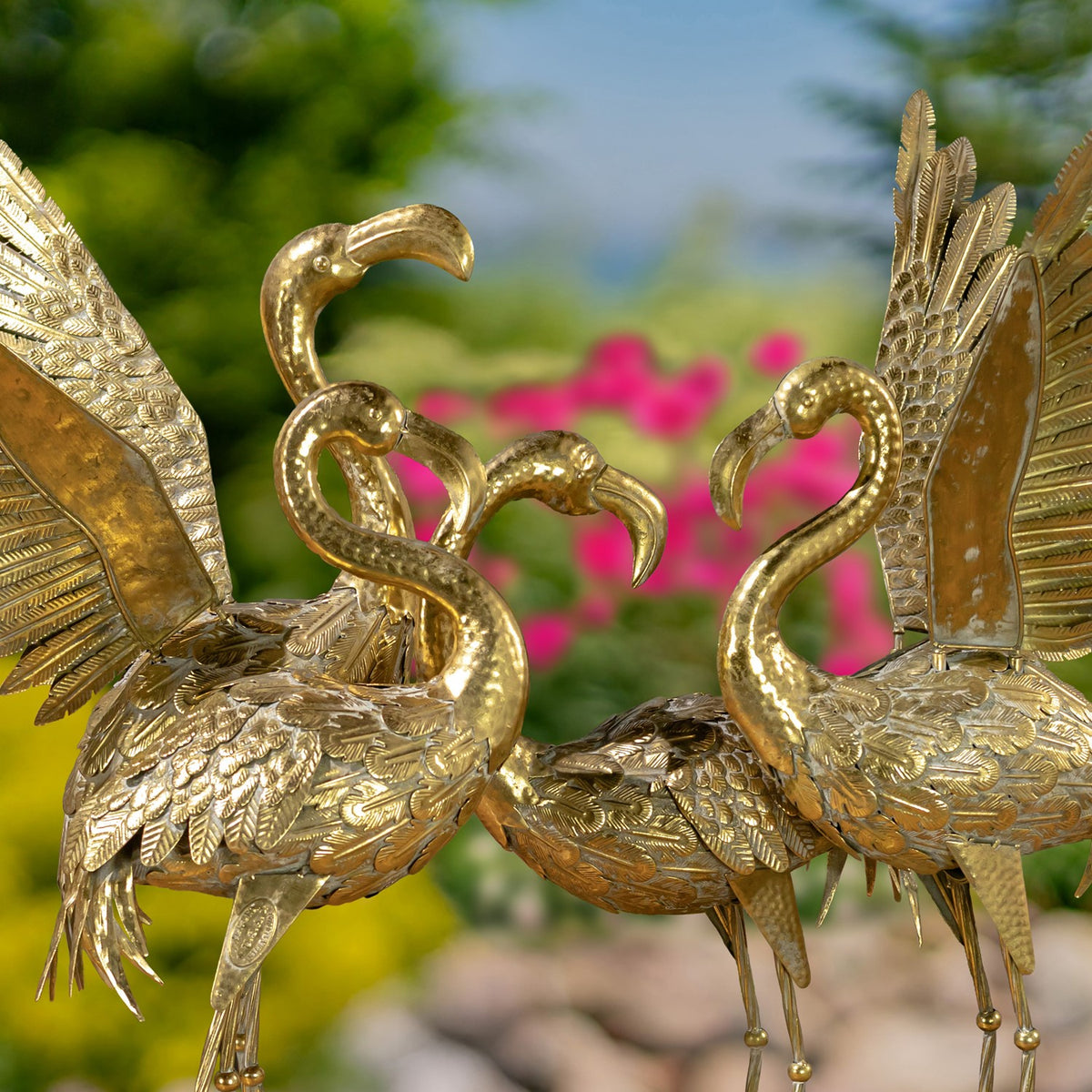 Close view of two ornate gold flamingo garden figurines with curved necks and raised wings.