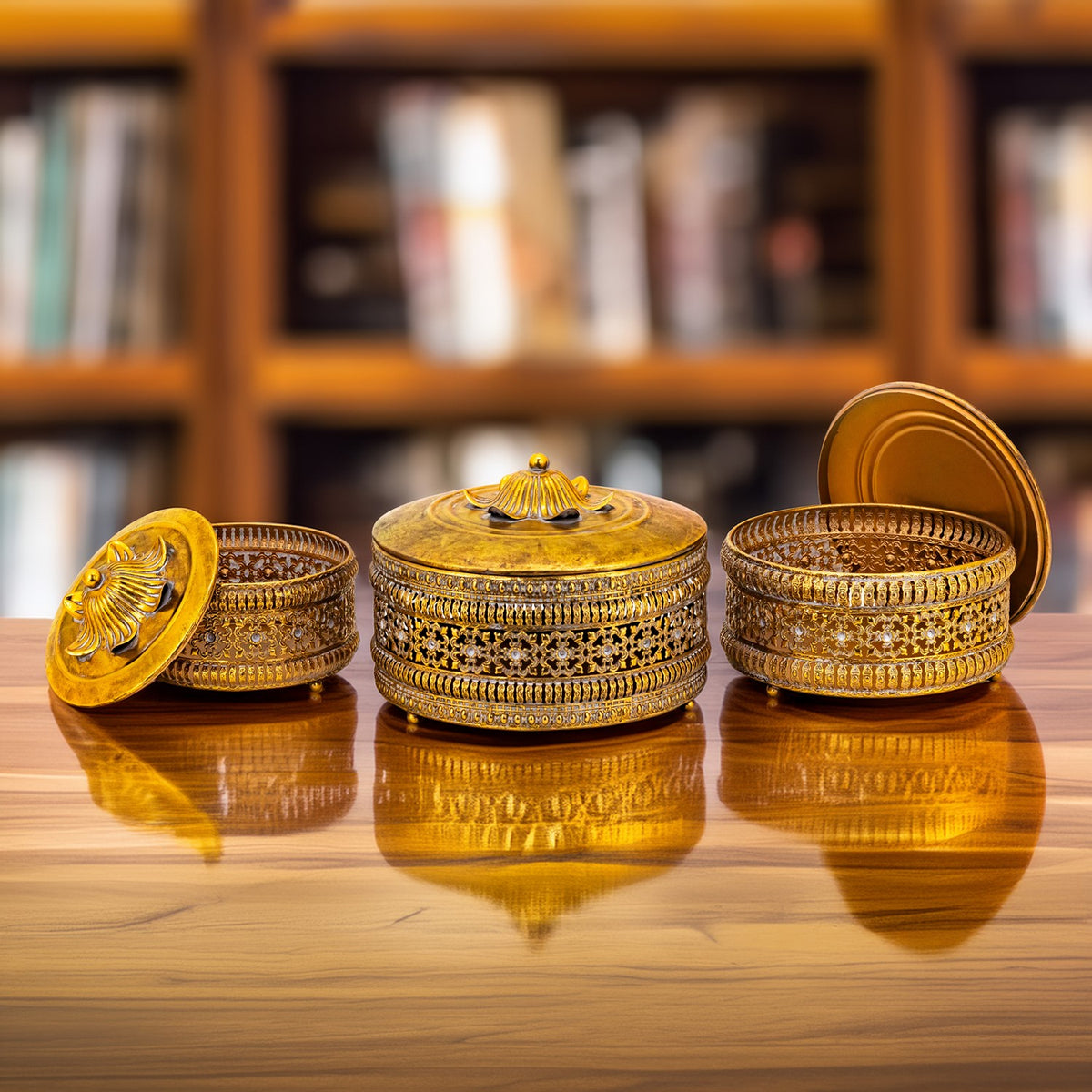 Three ornate gold-tone round boxes with domed lids arranged on a wooden tabletop.