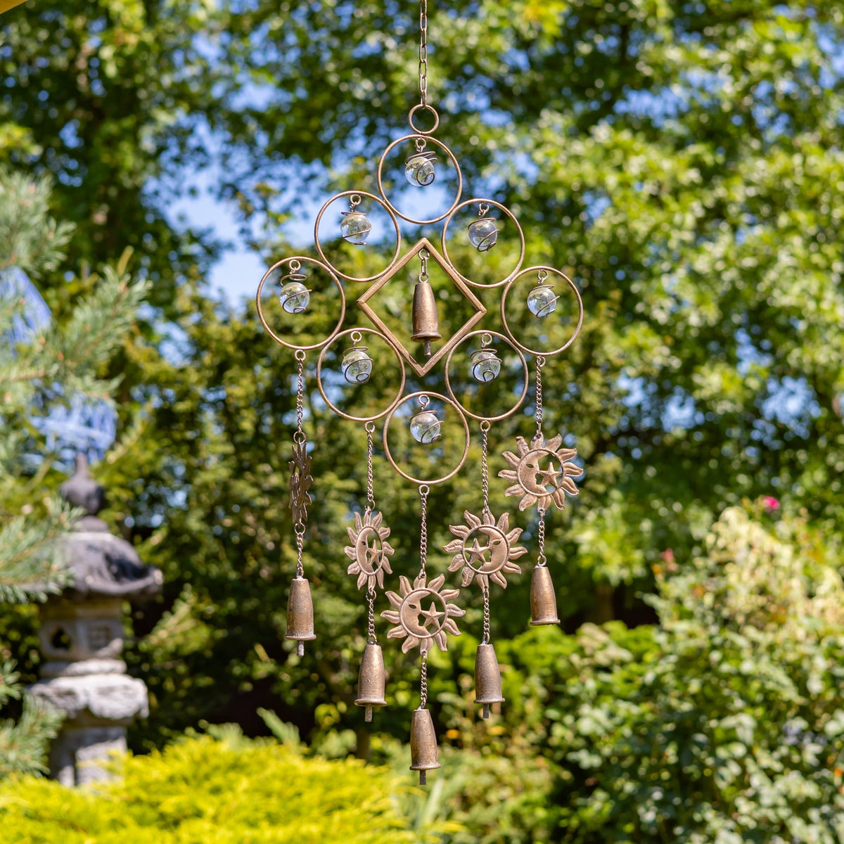 Metal wind chime with a circular and diamond-shaped frame, hanging bells, and sun ornaments outdoors.