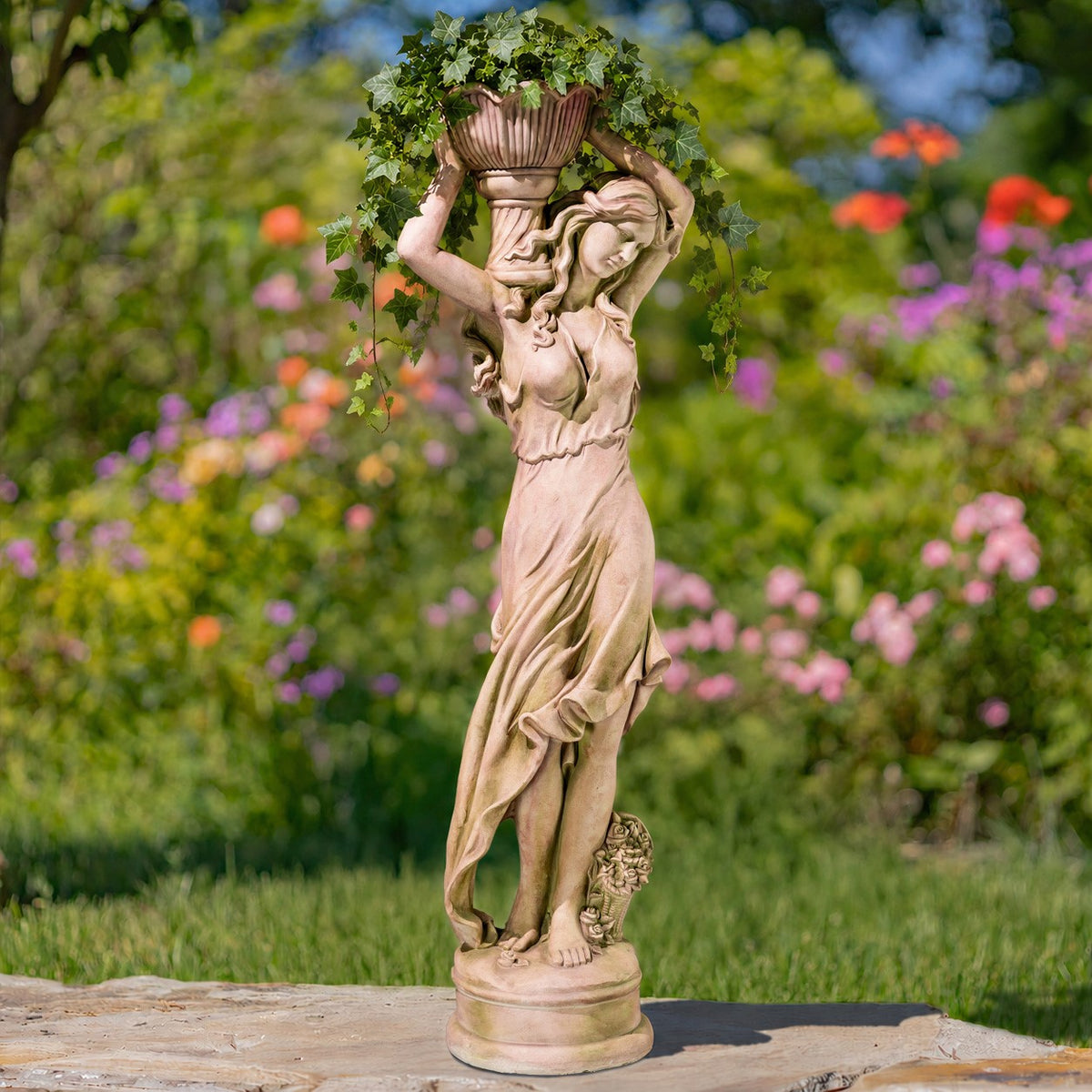 Full view of a draped female statue holding a leafy flower pot overhead, standing on a stone patio.