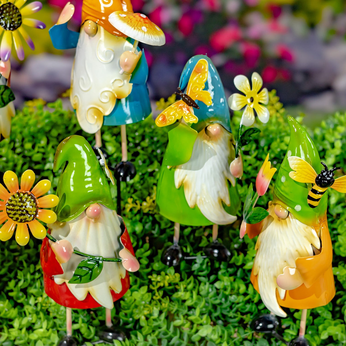 Colorful gnome garden stakes with flower and butterfly accents standing among green ground cover.