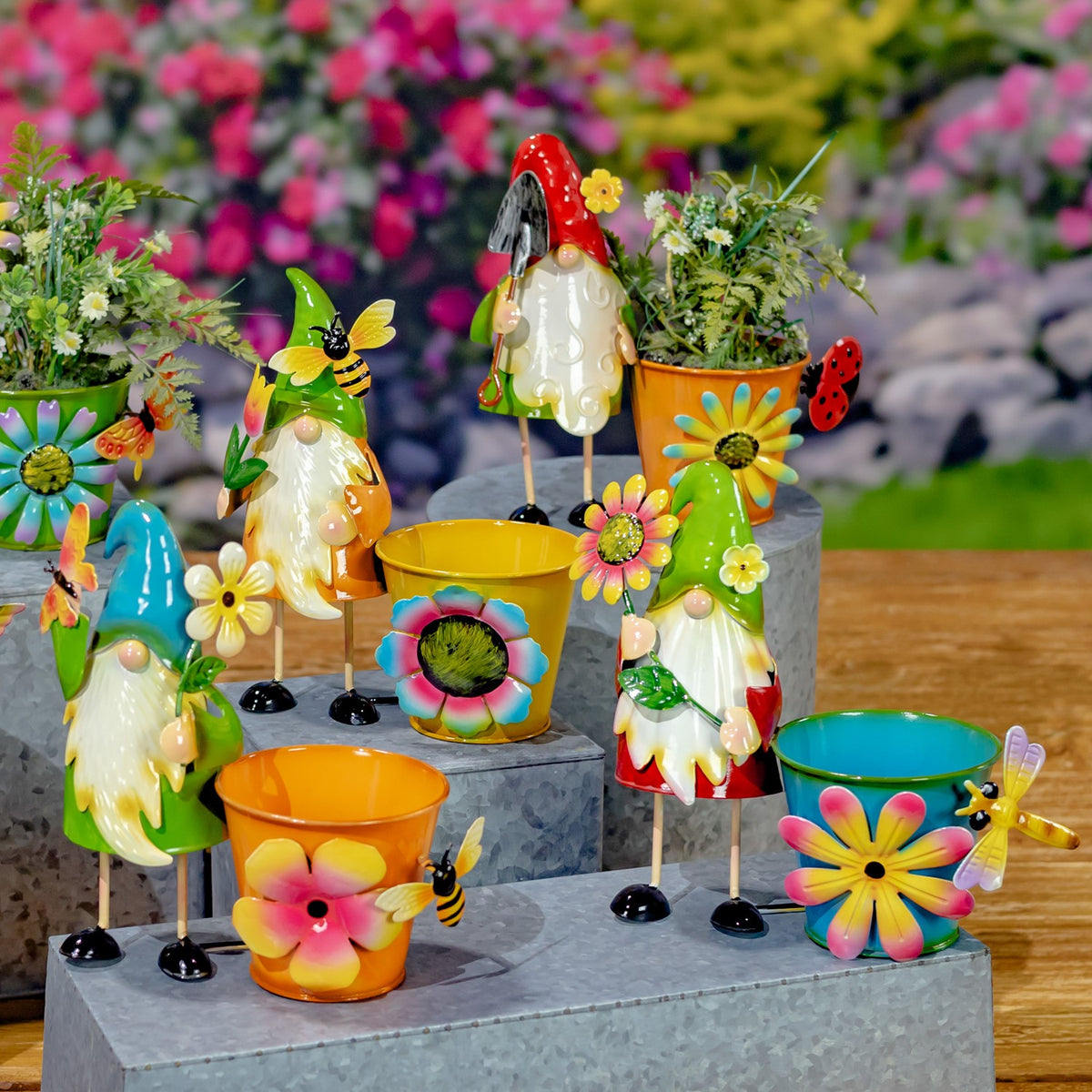 Colorful gnome-shaped flower pots and matching floral pots arranged on tiered stone blocks outdoors.