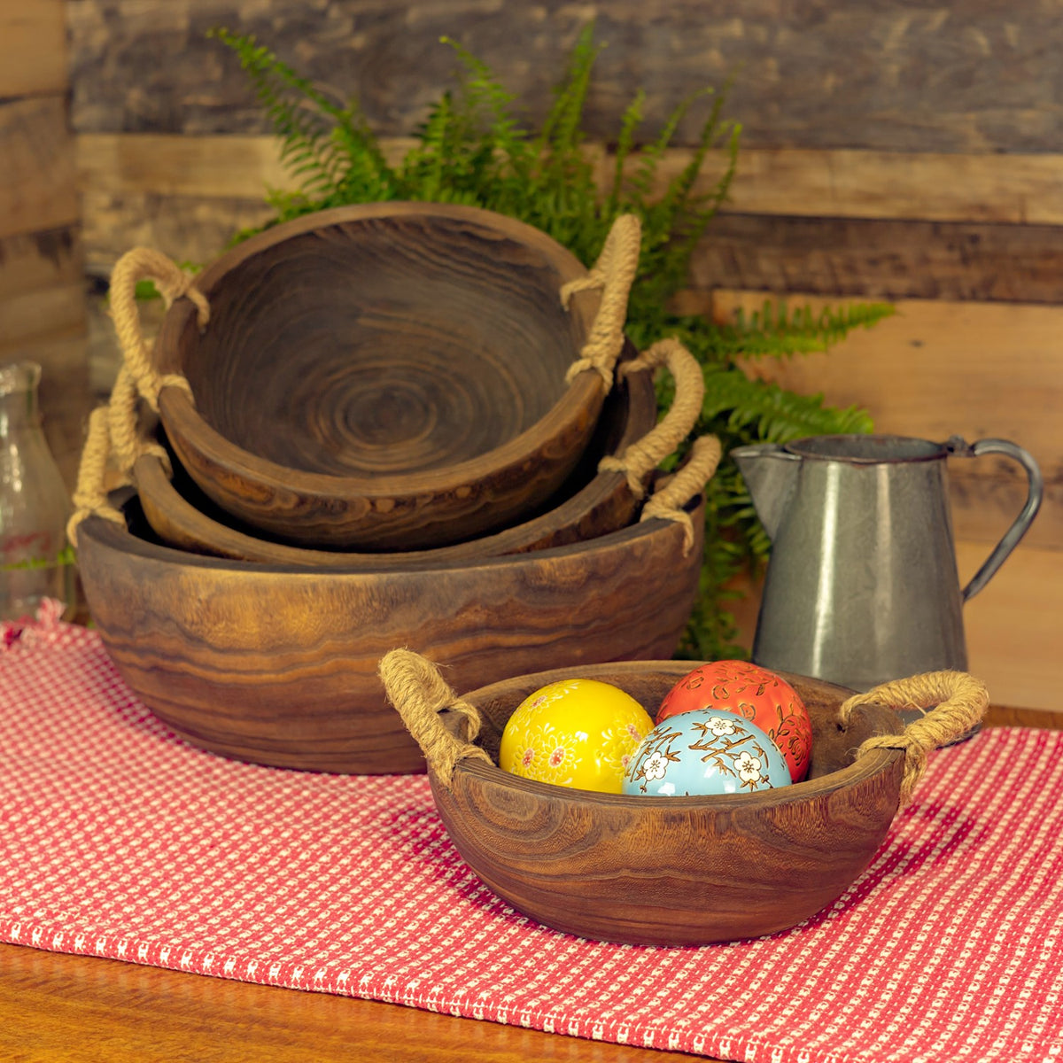 Four nested wooden trays with rope handles, with colorful eggs in the smallest tray on a table.
