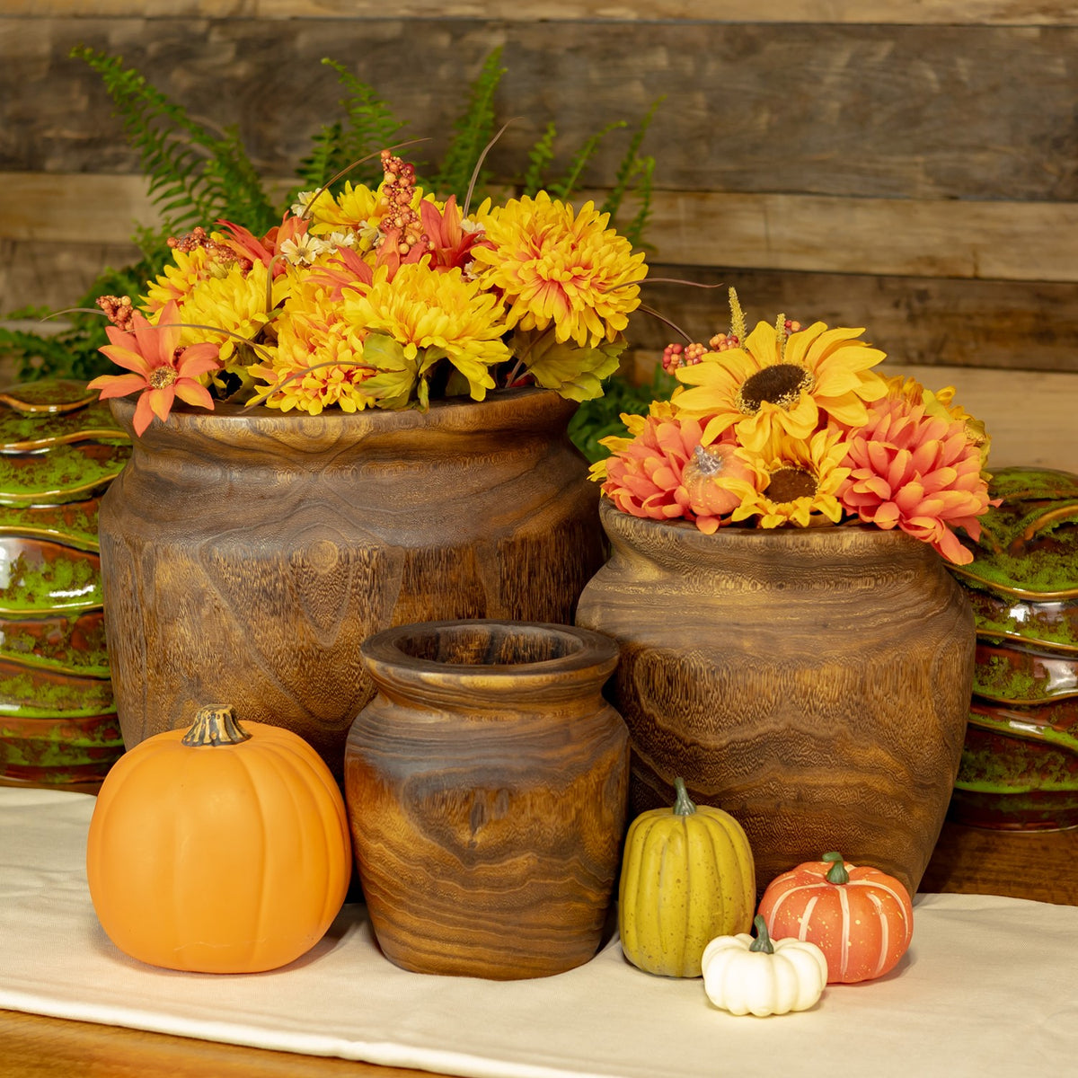 Three round brown planters arranged with autumn flowers and small decorative pumpkins.