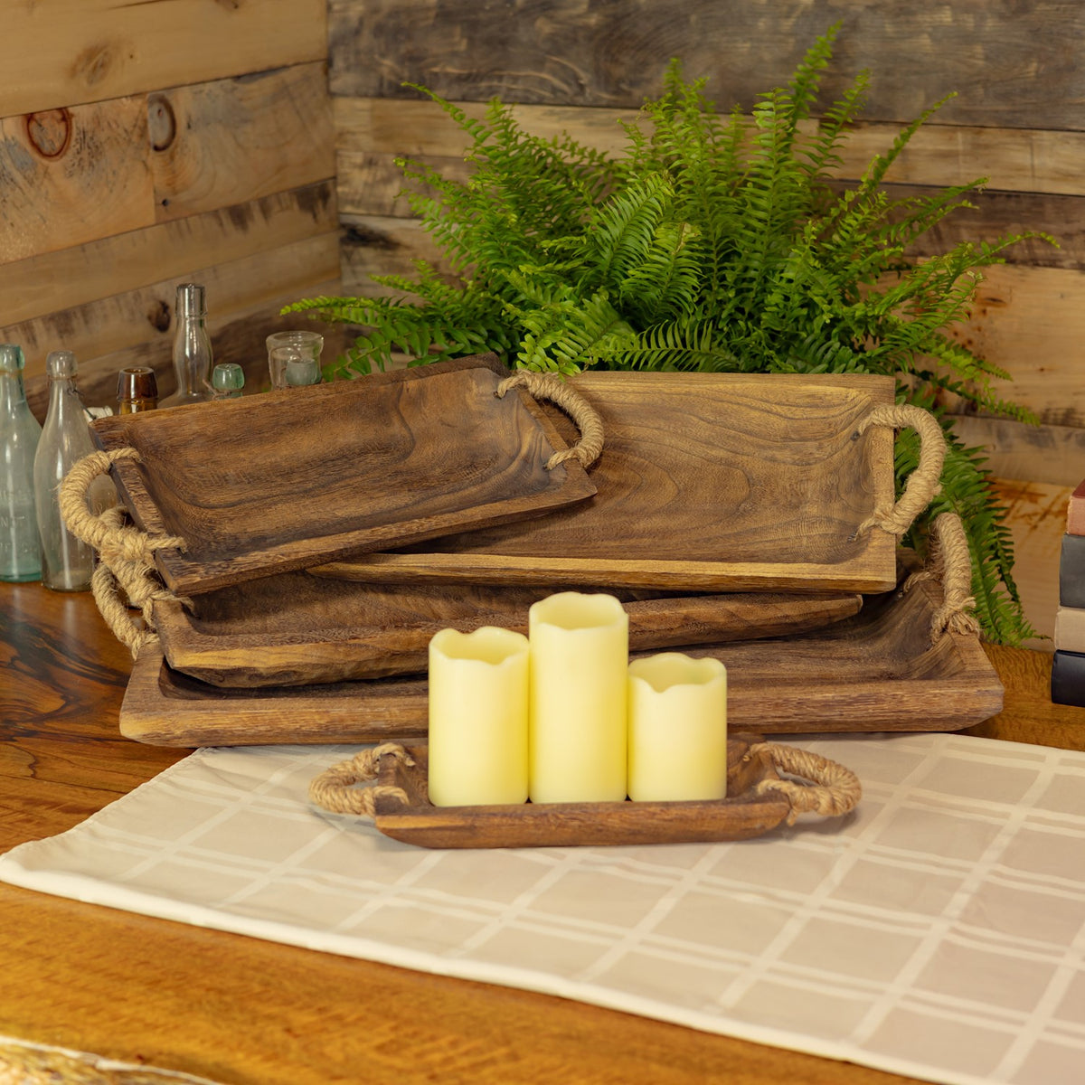 Stacked brown wooden trays with rope handles and candles on a table