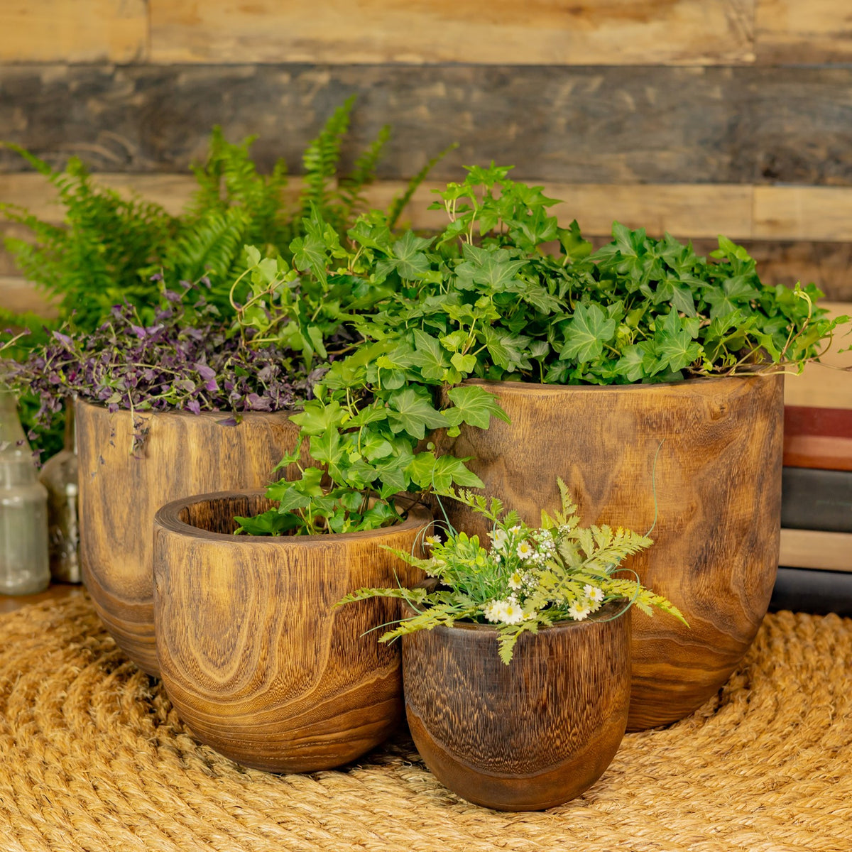 Four wooden bowls displayed as planters with greenery and flowers.