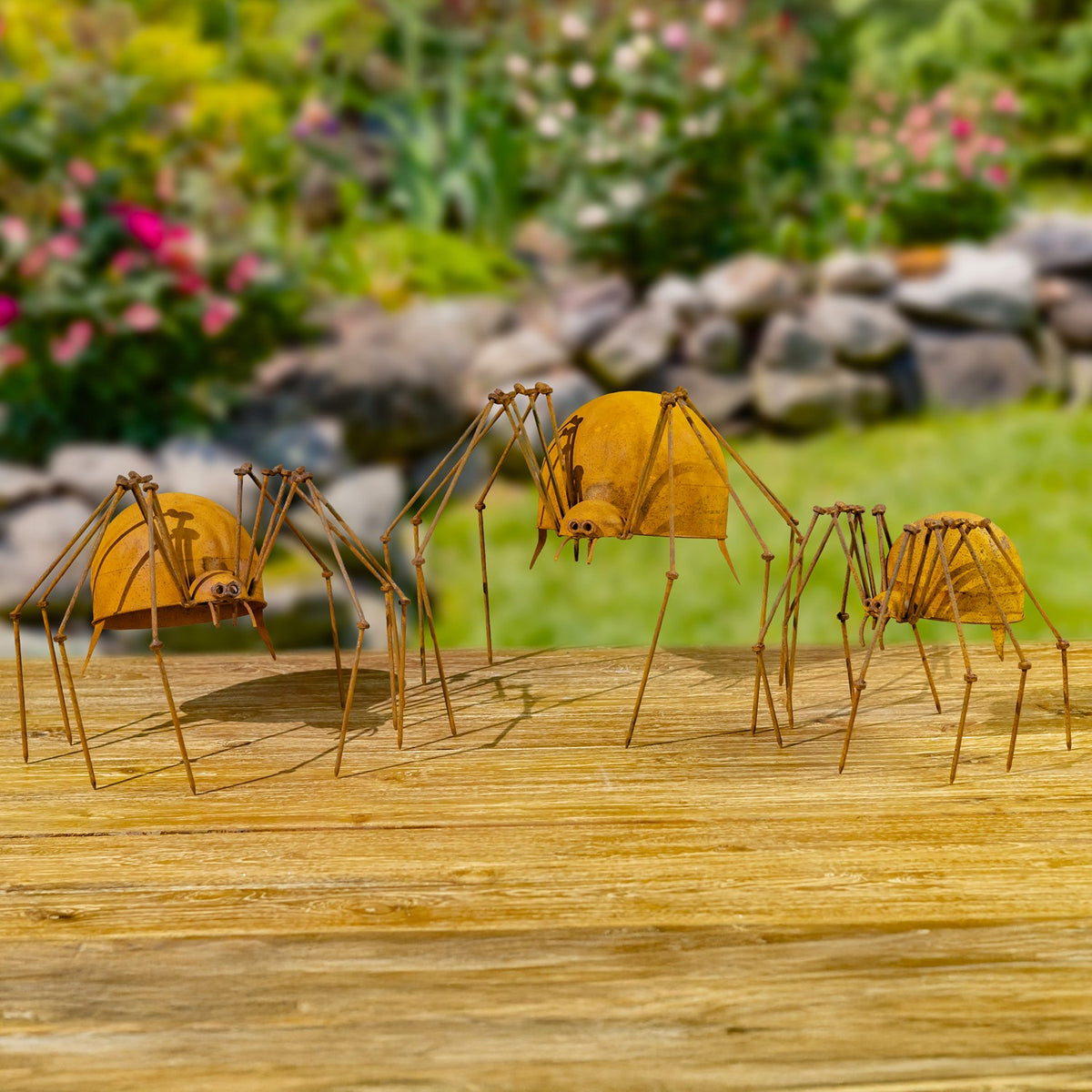 Three rust-finish iron spider figurines on a wooden surface in a garden