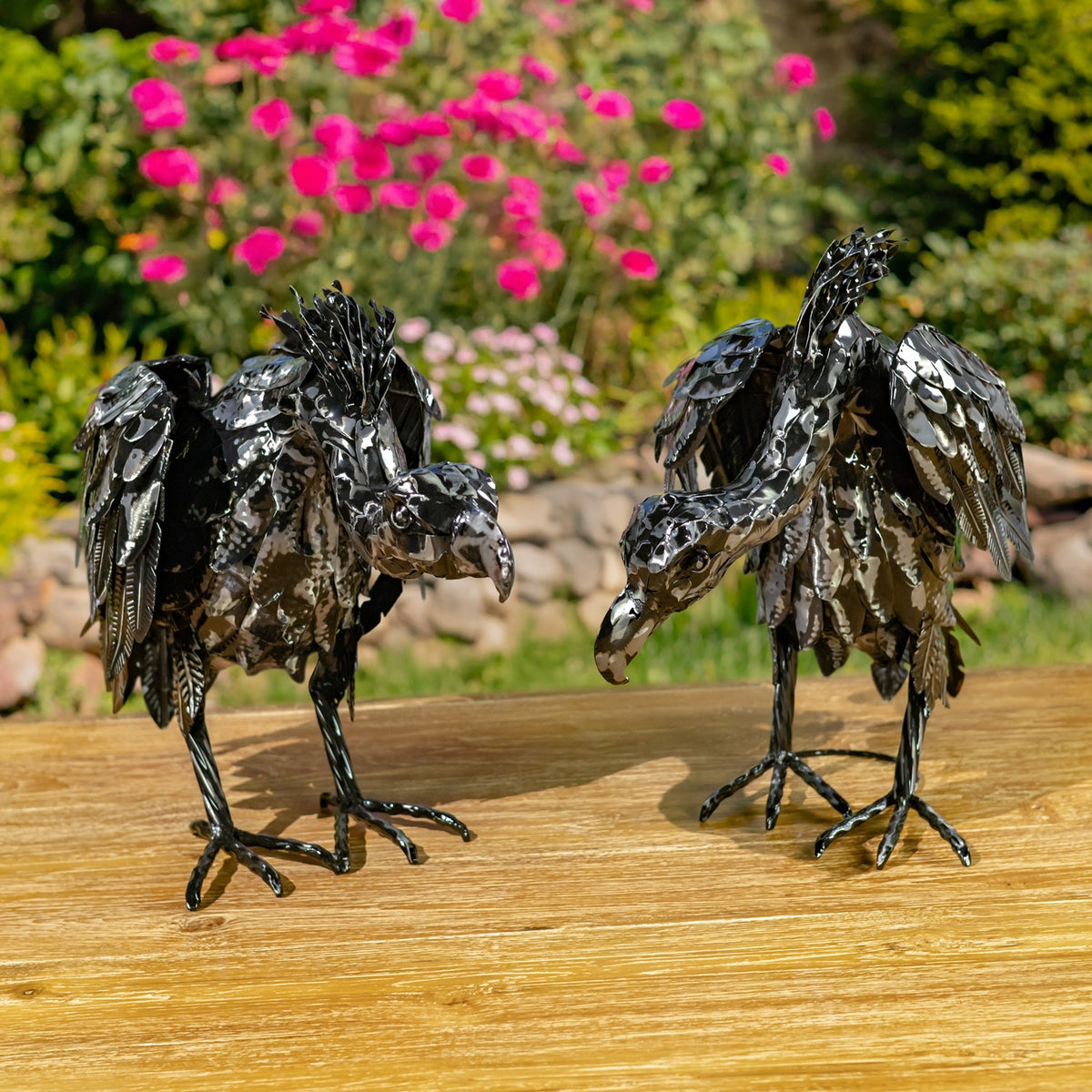 Two metallic black vulture figurines standing on a wooden table in a garden