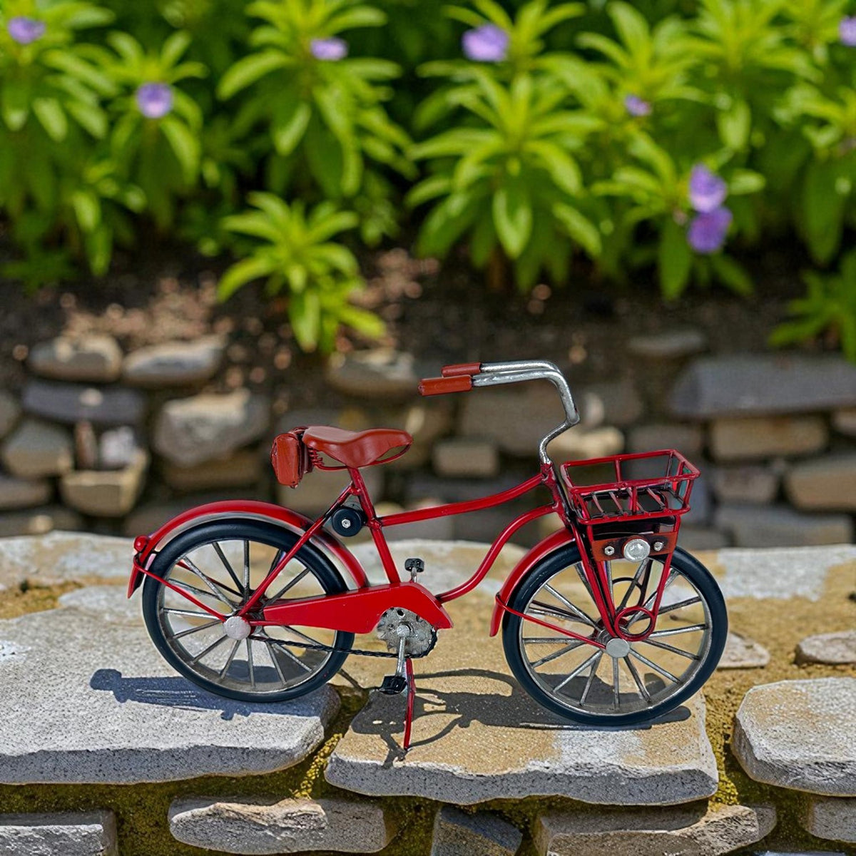 Red vintage-style miniature bicycle with a front basket displayed on stone pavers outdoors.