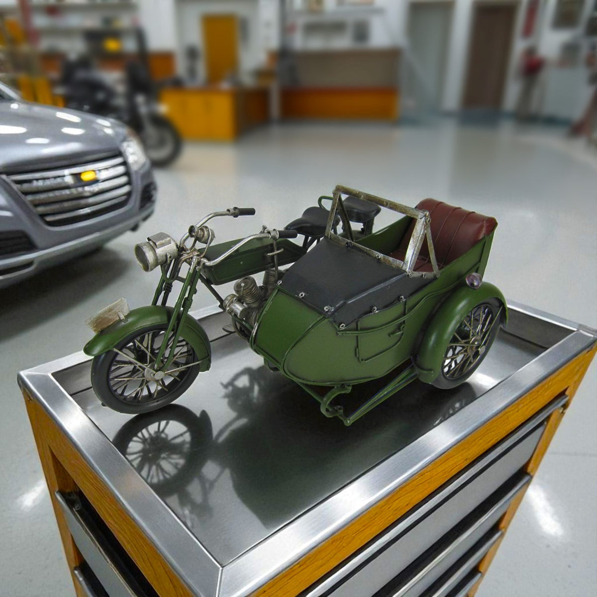 Army-green metal motorcycle with a side cart and brown seat, displayed on a counter.