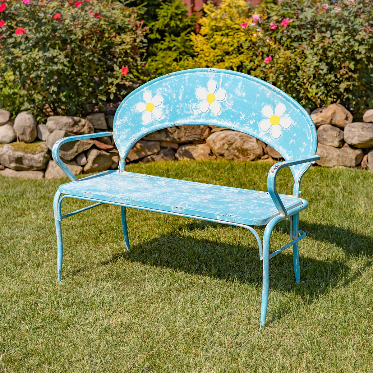 Distressed blue metal garden bench with white and yellow flower accents, shown on grass.