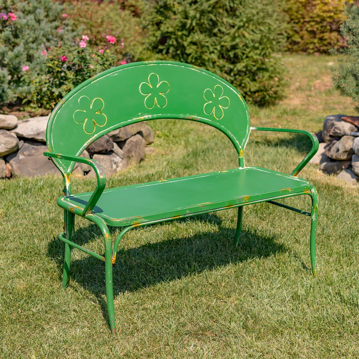 Green metal garden bench with gold flower outlines and gold trim on a lawn.
