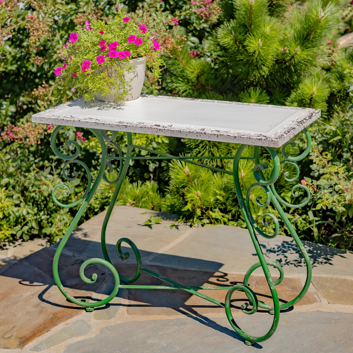 White tabletop with a distressed edge on a green curled iron frame, with a flowerpot on top.