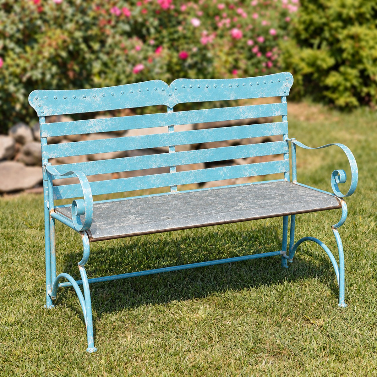 Blue metal garden bench with a dark seat and curled arms stands on a lawn.
