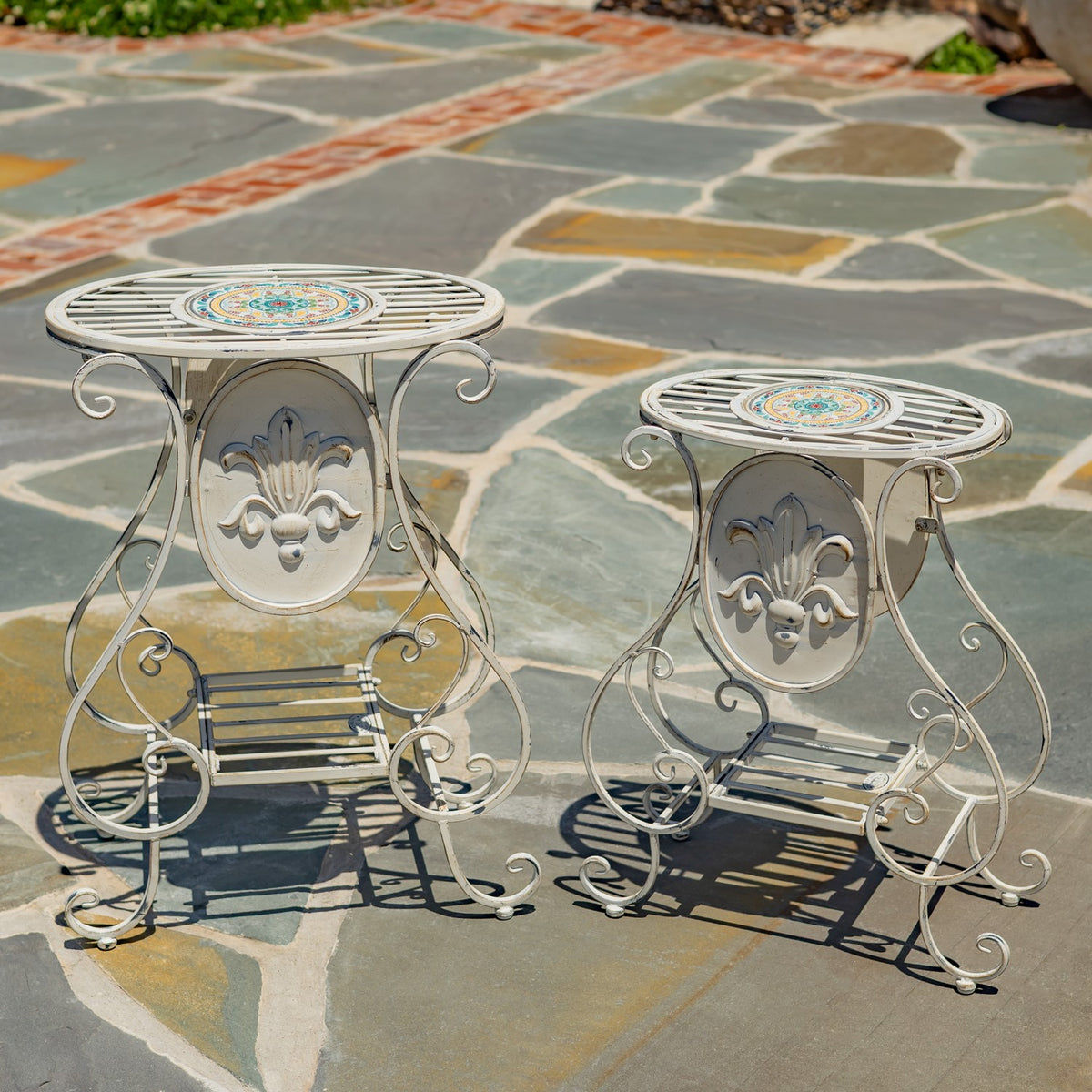 Two ornate cream plant stands with colorful mosaic centers sit on a stone patio.