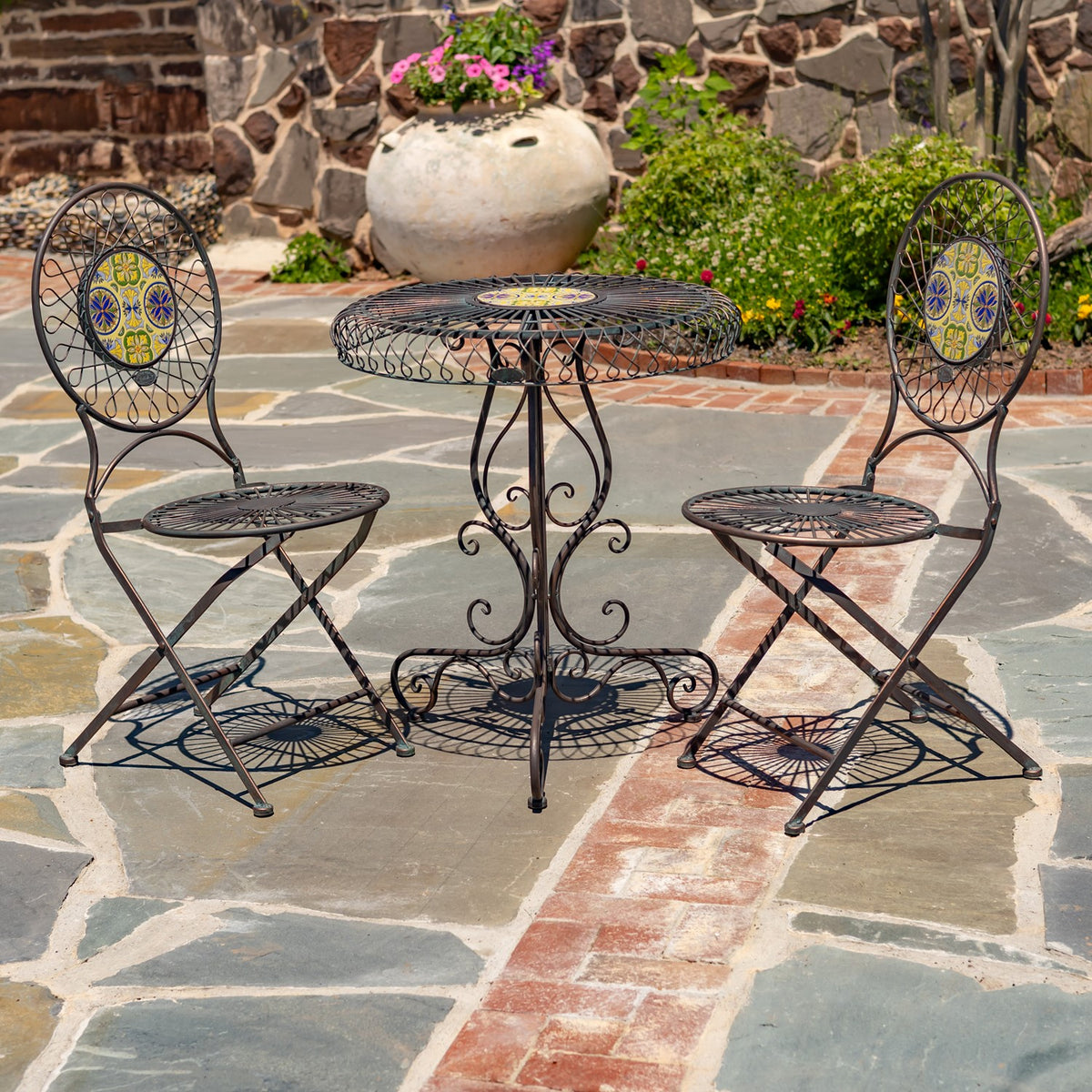 Round mosaic-top bistro table with two matching wire-frame chairs on a stone patio.