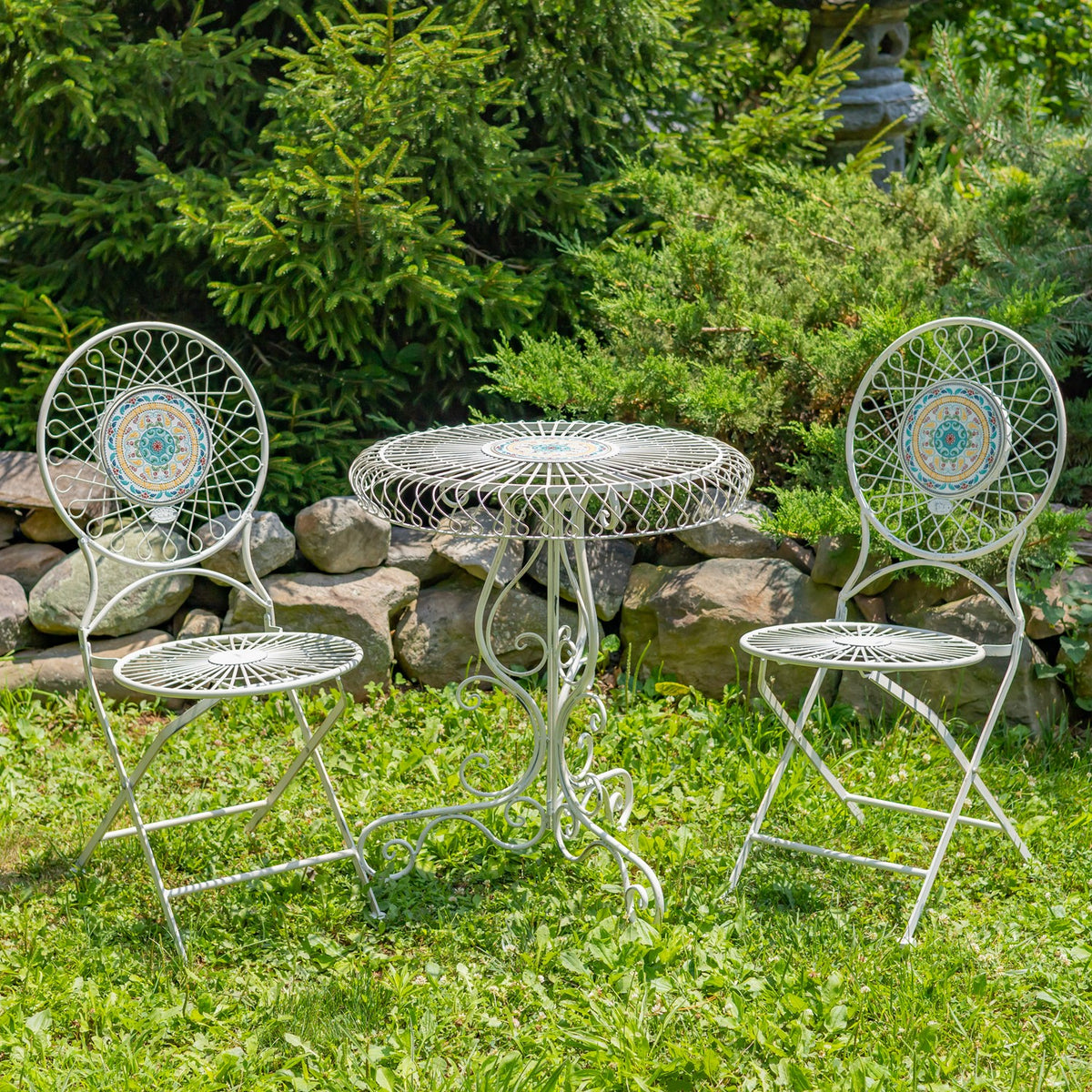 White wire bistro table and two matching mosaic-backed chairs arranged on a grassy garden lawn.