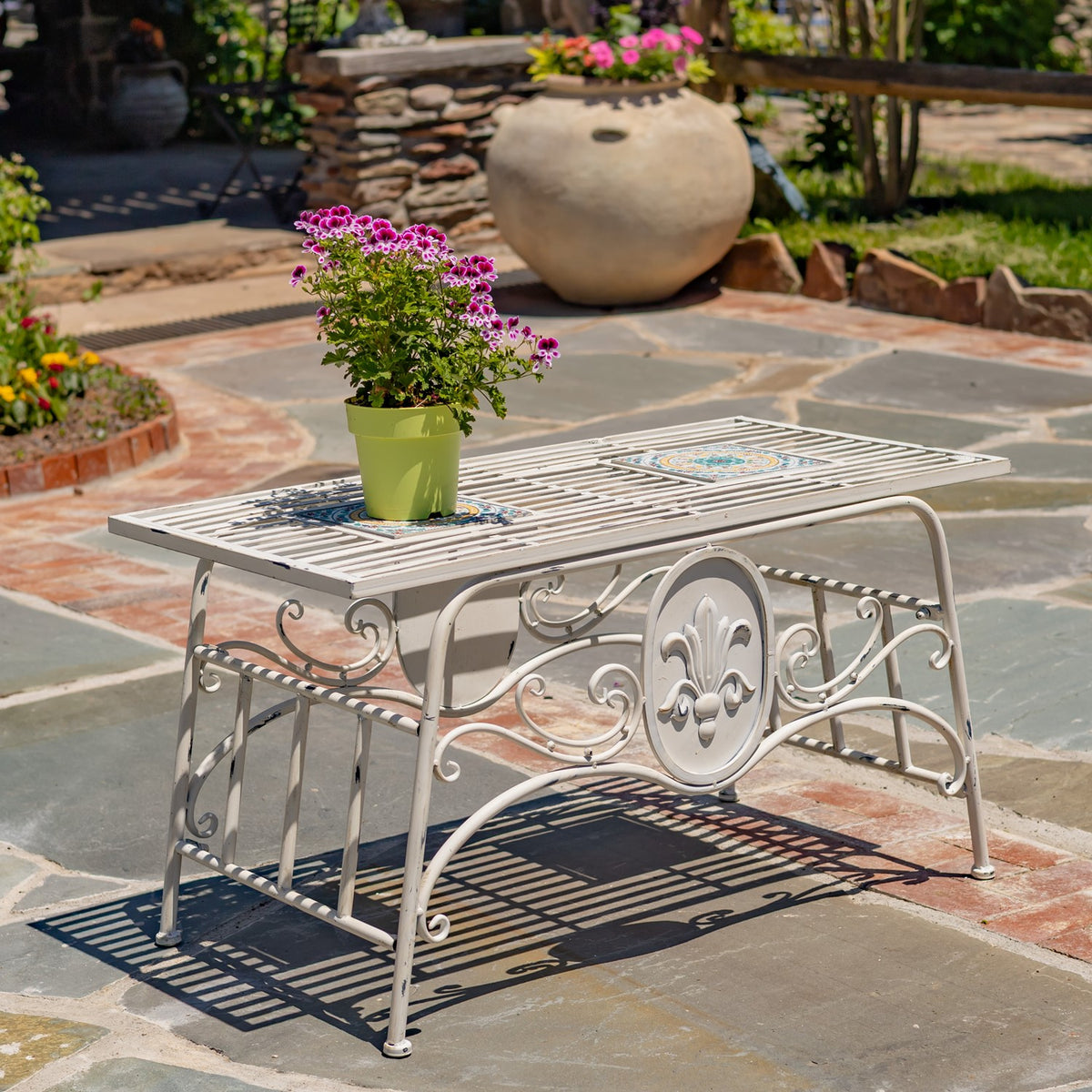 White rectangular mosaic-top metal table with a potted flower in a garden patio setting.