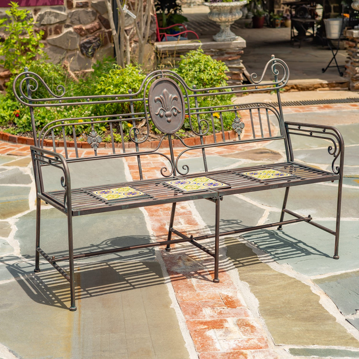 Ornate metal garden bench with mosaic seat tiles on a multicolored stone patio.