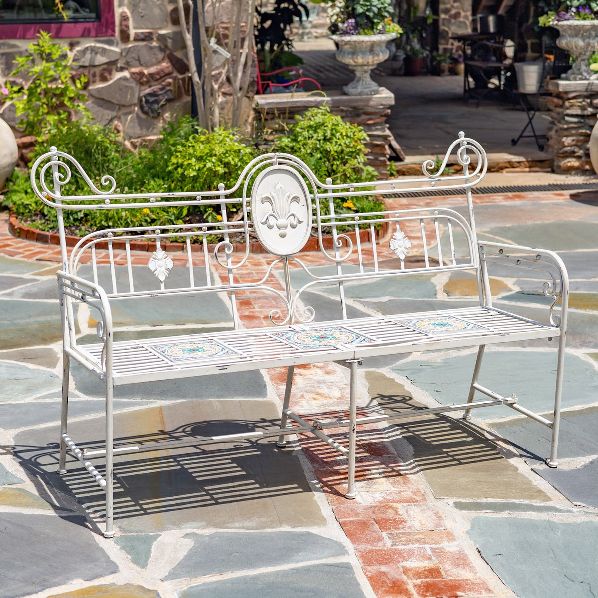 Ornate white metal garden bench with mosaic seat tiles on a stone patio