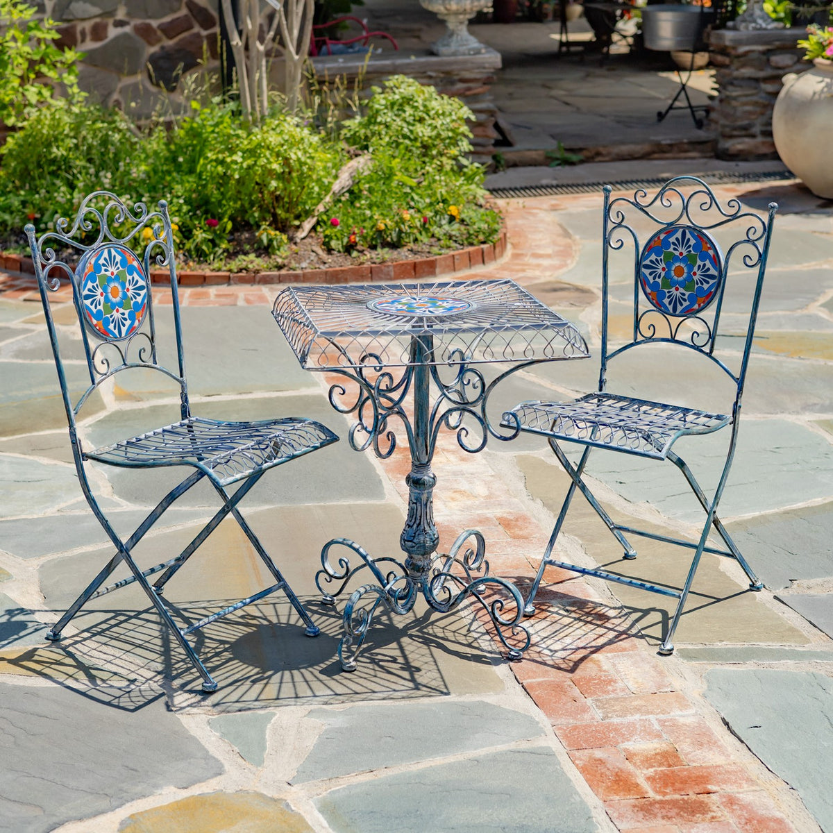 Blue wrought-metal bistro table and two matching mosaic-back chairs on a stone patio.