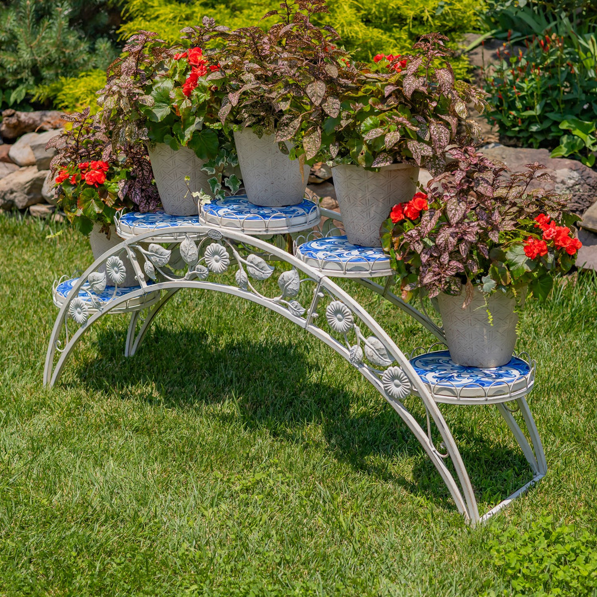 Antique-white arched plant stand with blue mosaic shelves holding several potted plants on a lawn.