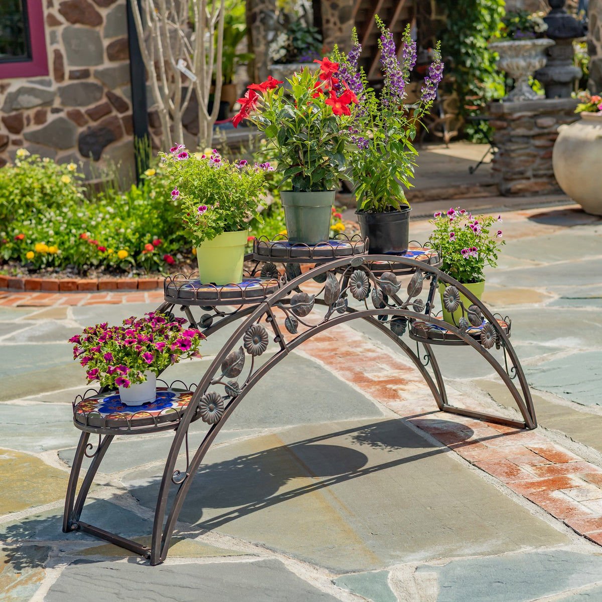 Arched bronze-toned plant stand filled with potted flowers on a stone patio.