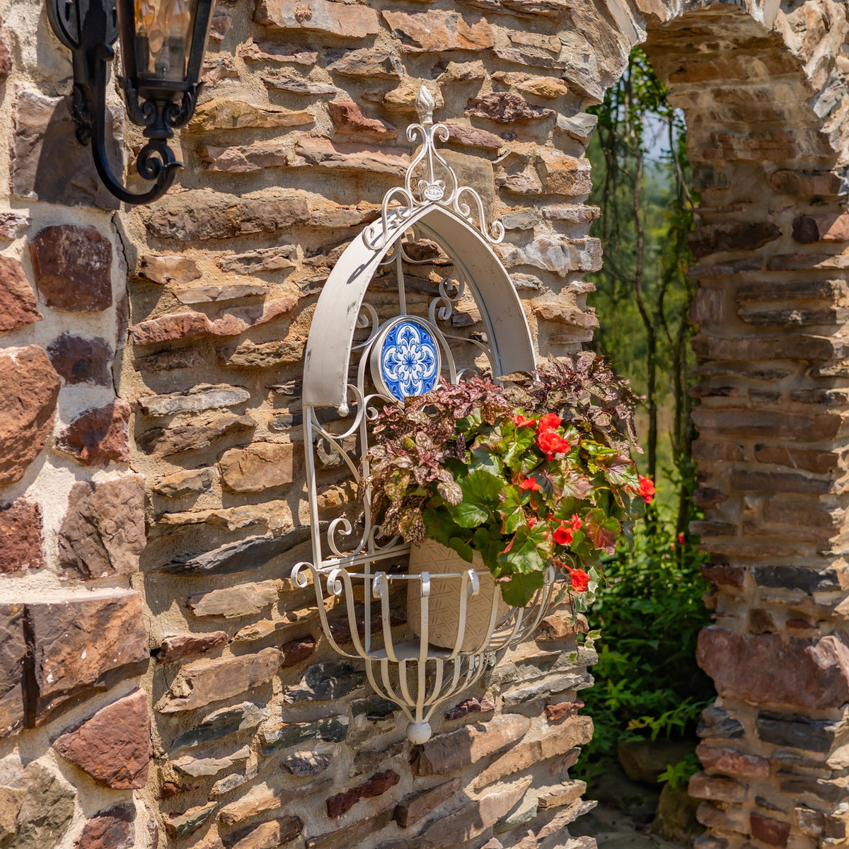 Ornate white wall planter filled with flowers against a stone wall, with a lantern above.