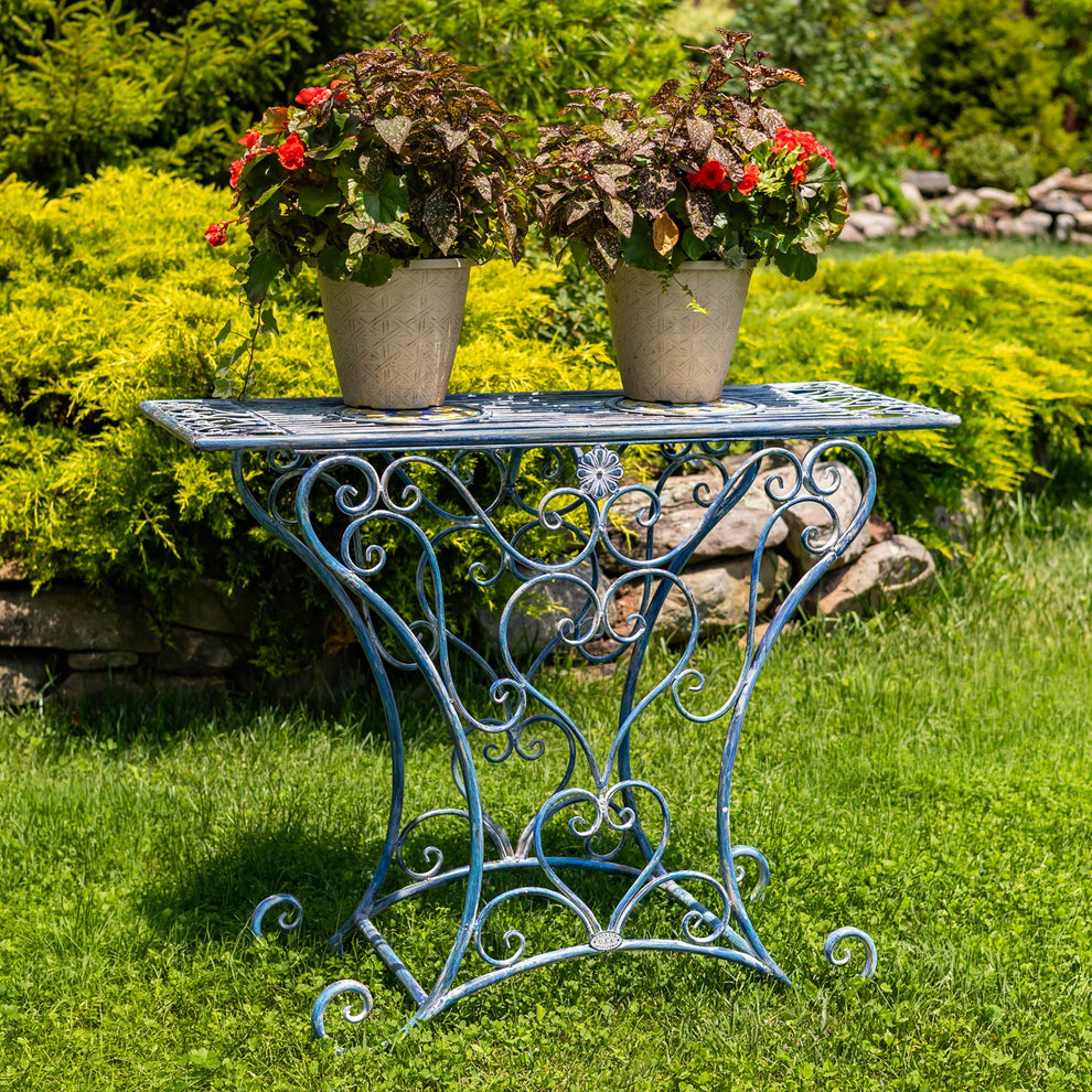 Blue mosaic-top iron table with ornate scrollwork legs, shown outdoors with two flower pots on top.